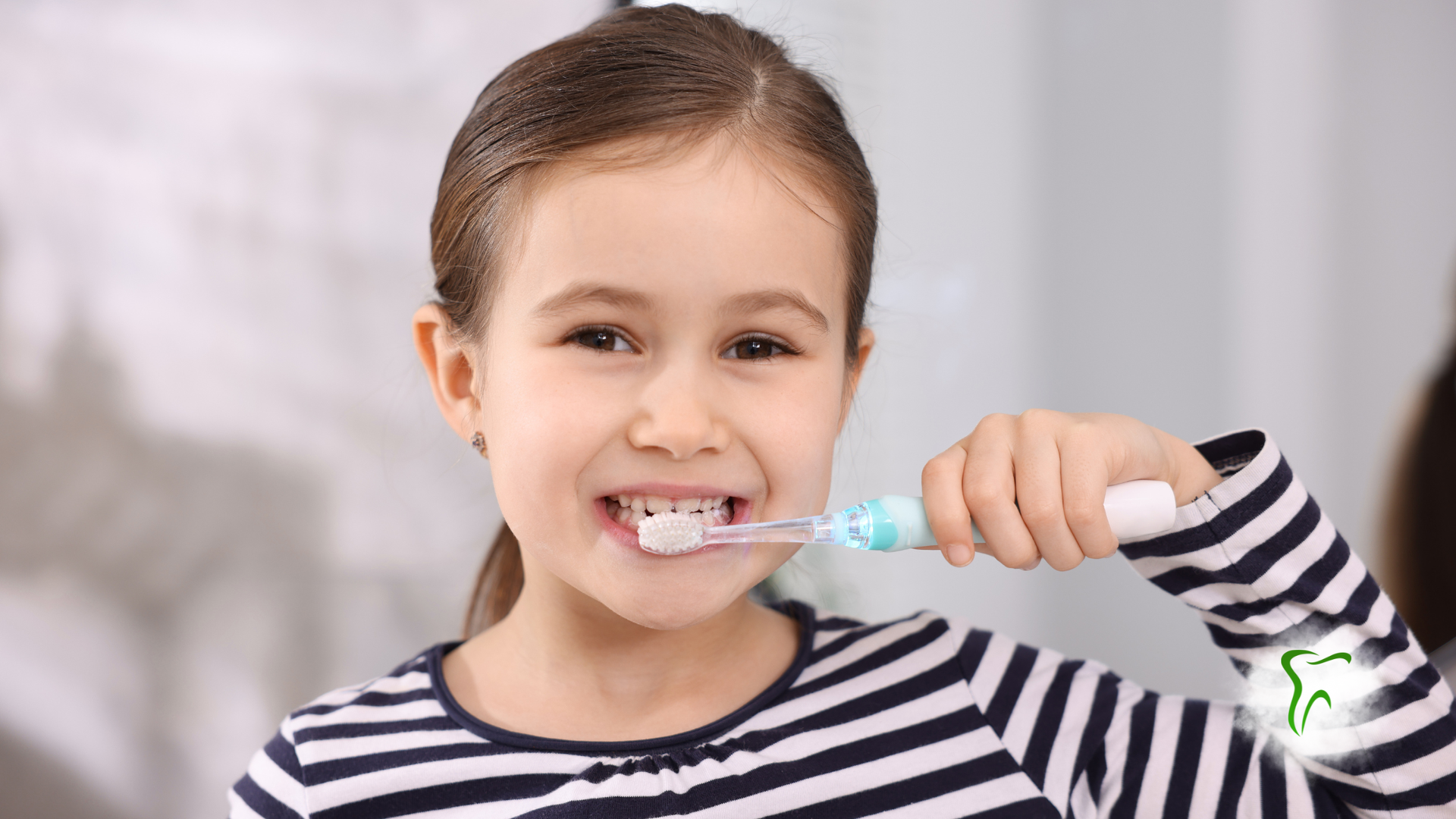 Girl brushing teeth with an electric toothbrush in a bathroom, smiling.