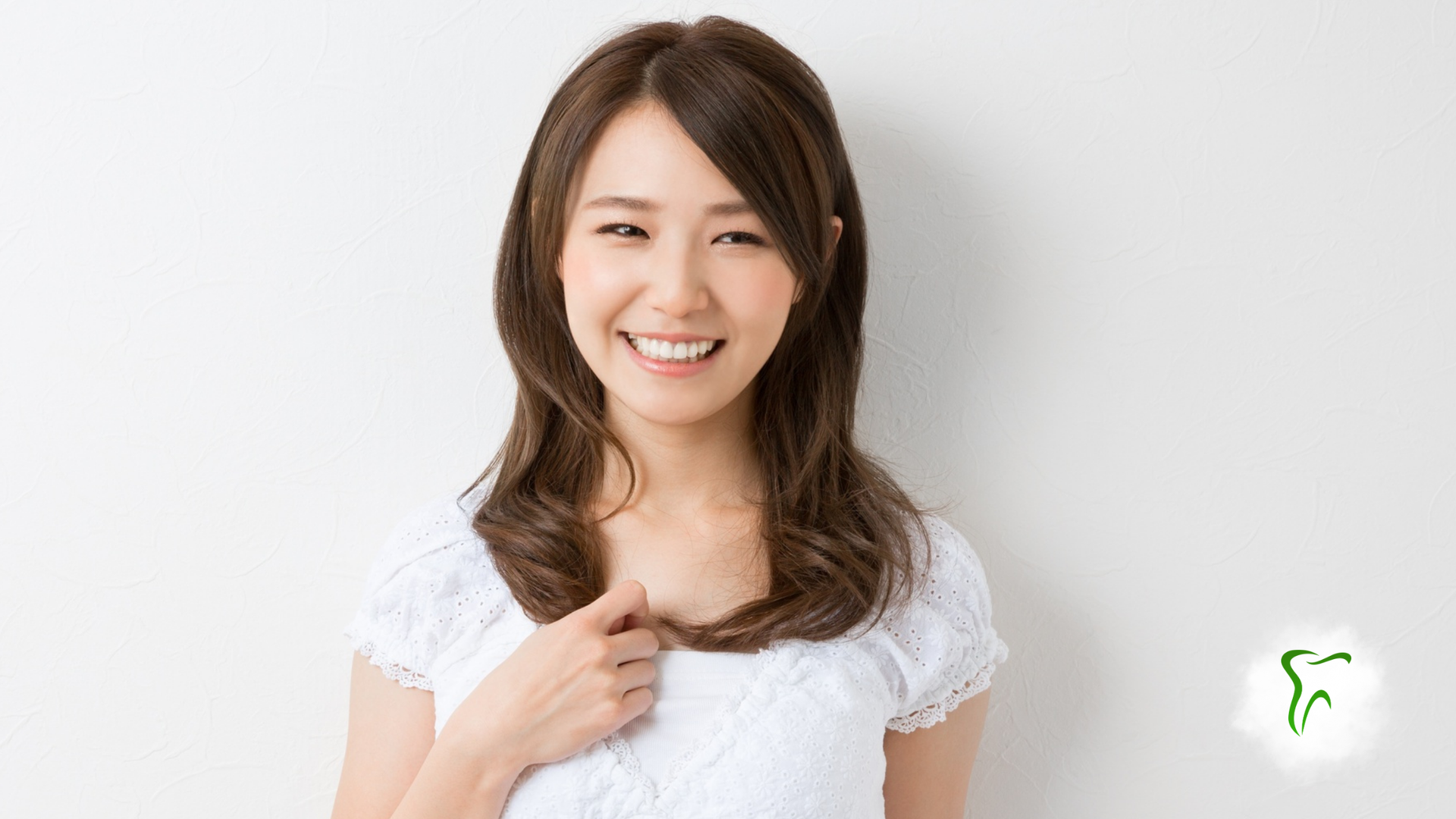 Smiling woman in a white top against a light background, pointing to herself.
