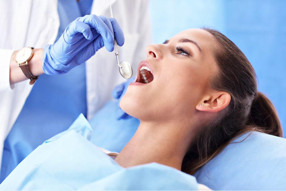 A woman is sitting in a dental chair while a dentist examines her teeth.