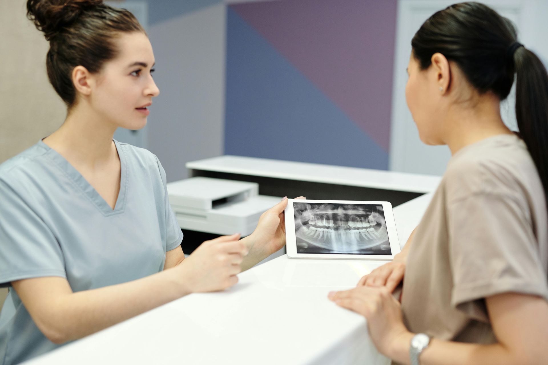 A dentist is showing a patient an x-ray of her teeth on a tablet.