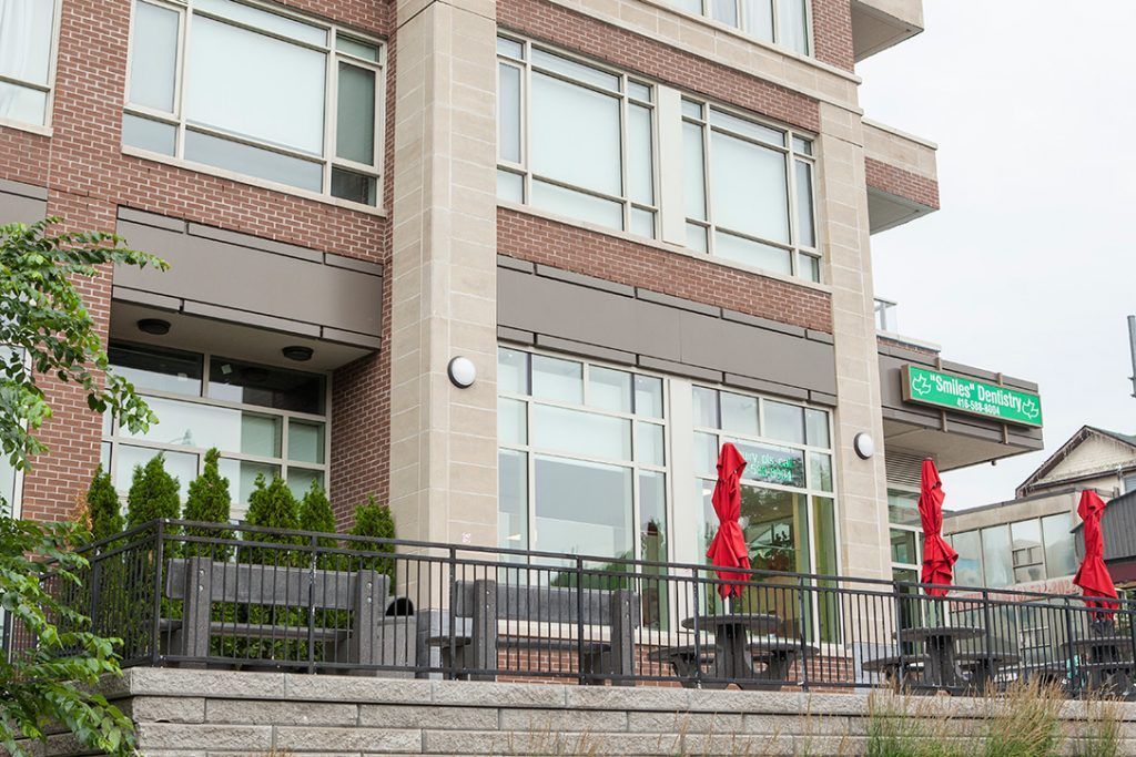 A large brick building with a balcony and red umbrellas in front of it.