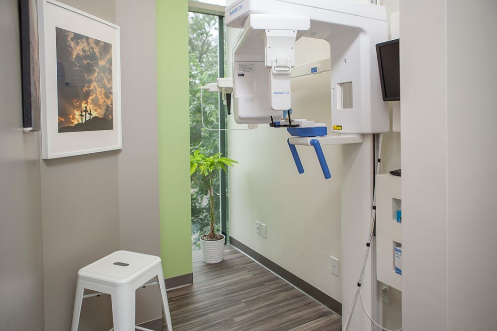 A dental office with a stool and a x-ray machine.