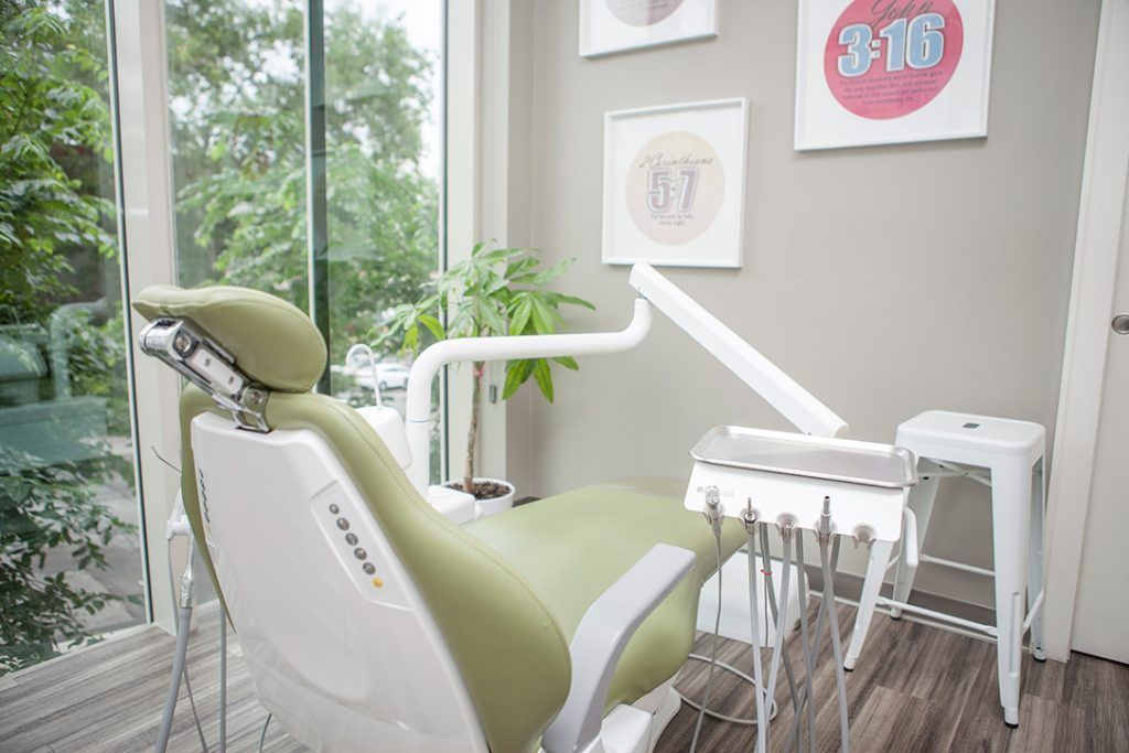 A green dental chair is in a dental office next to a window.