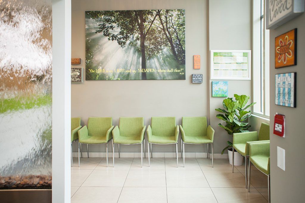 A waiting room with green chairs and a picture on the wall.