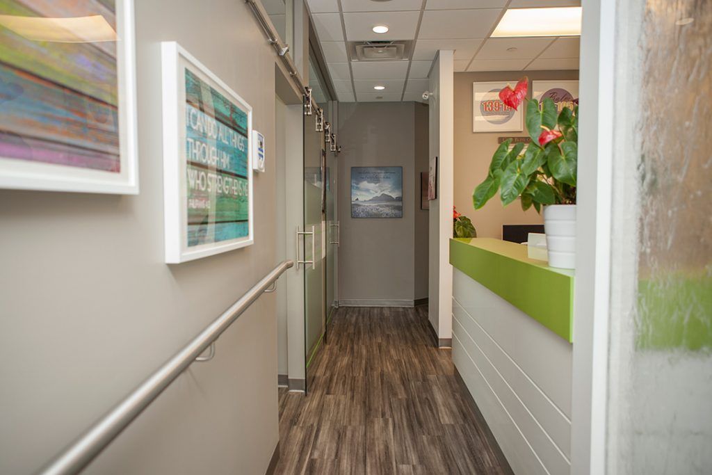 A long hallway in a hospital with a green counter and paintings on the wall.