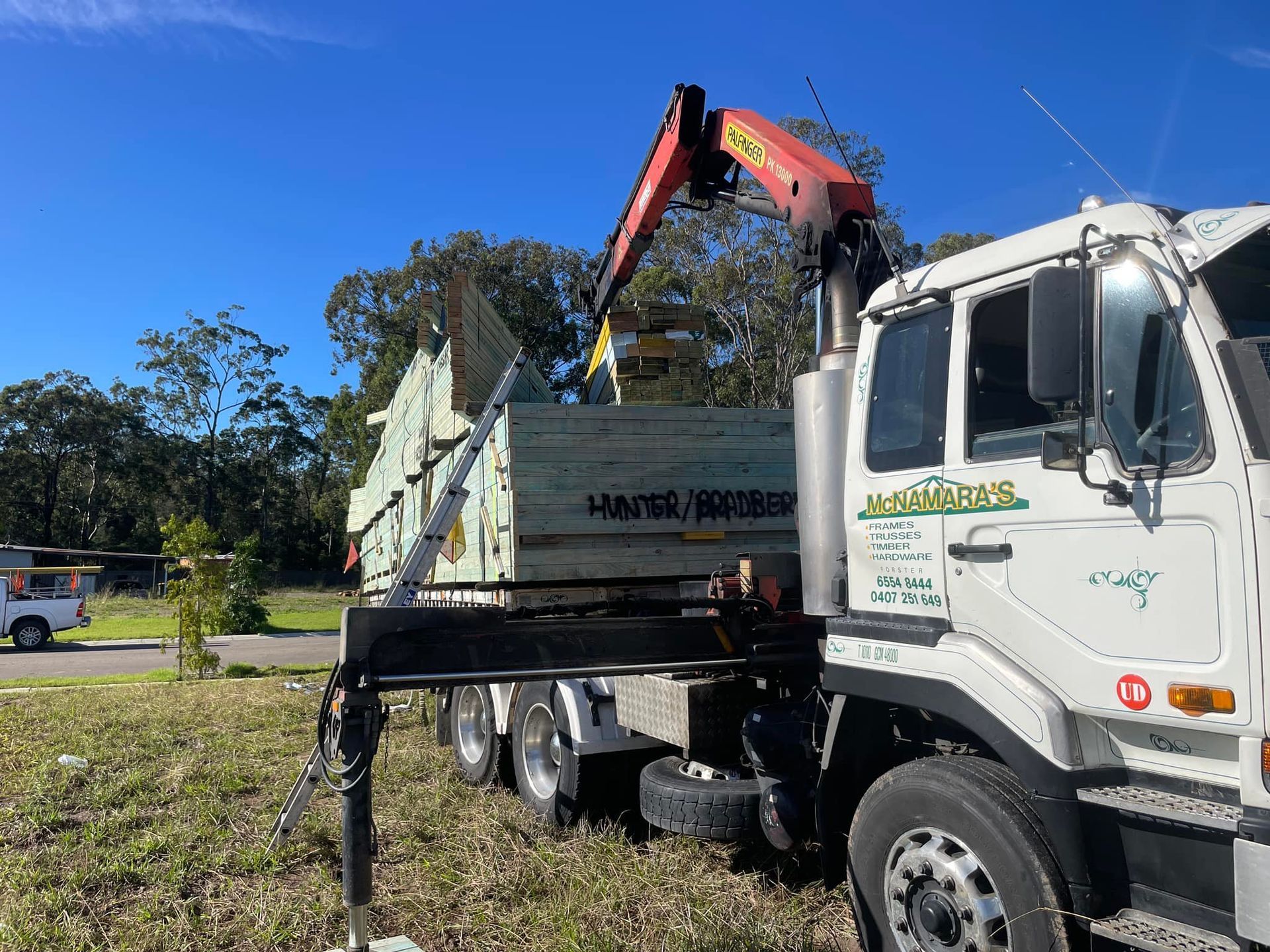Truck With Crane Unloading Lumber at a Construction Site — McNamara's Frames & Trusses In Forster, NSW