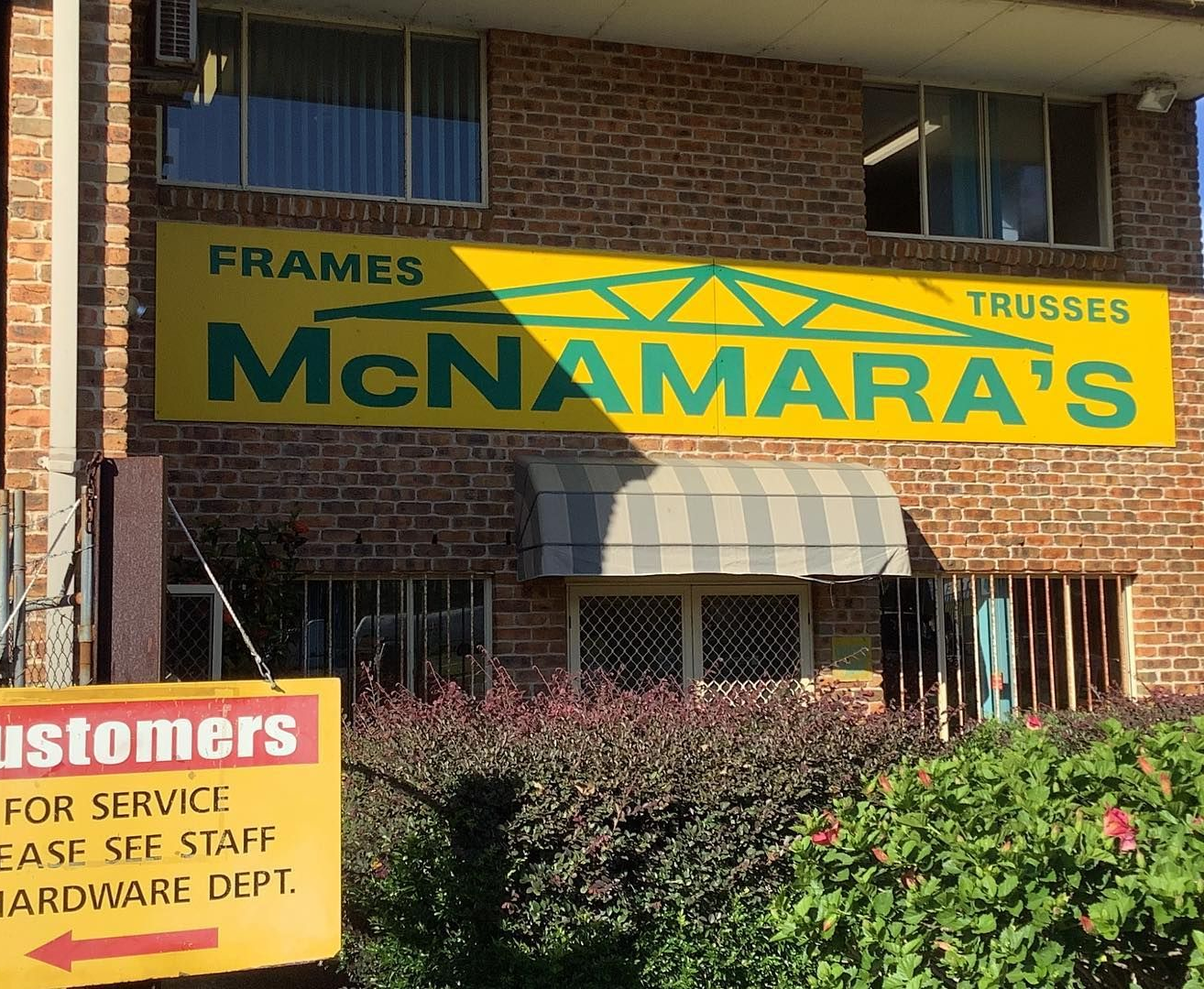 Green and Yellow Sign Over a Brick Building — McNamara's Frames & Trusses In Forster, NSW