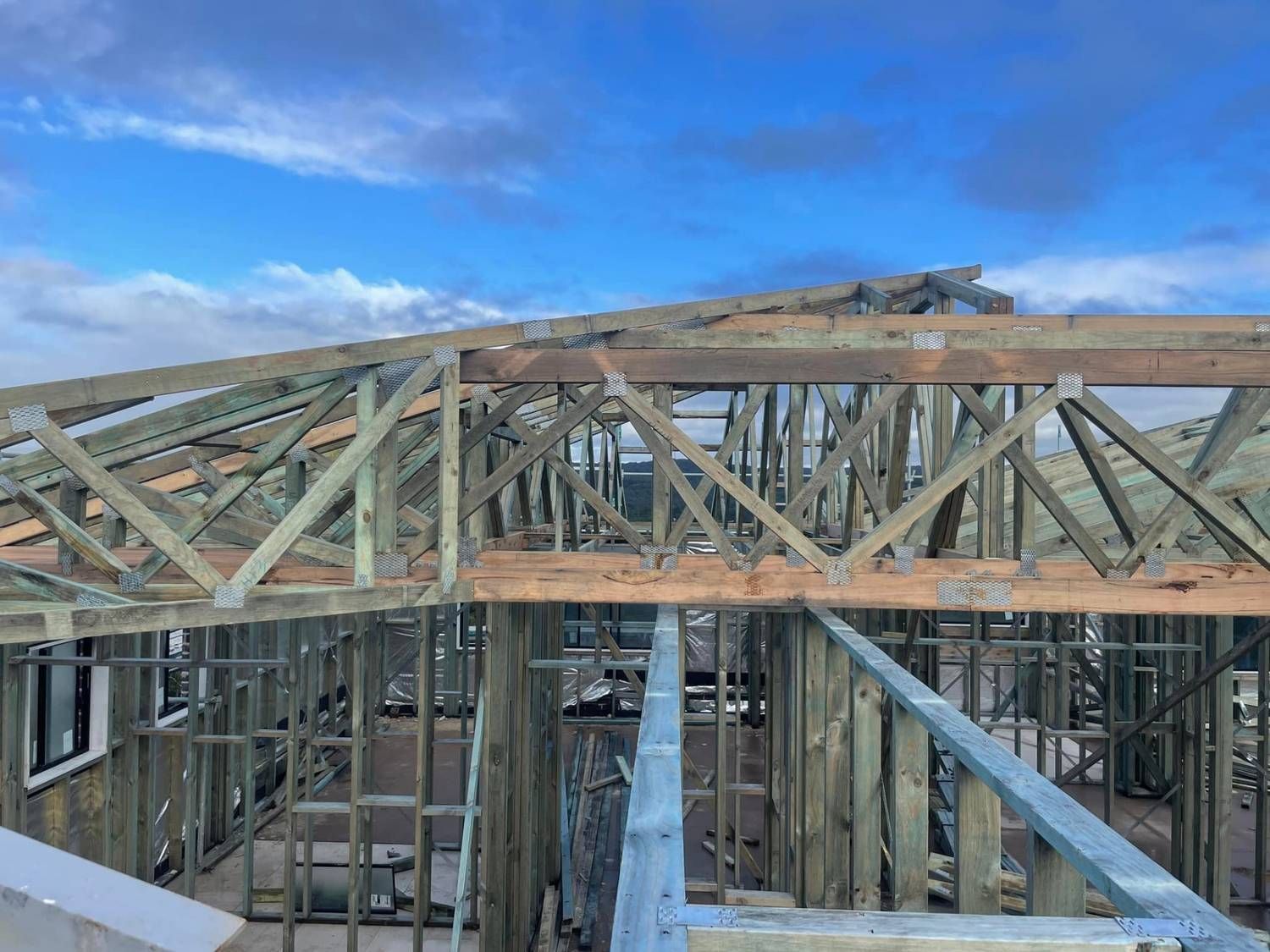 Wooden Roof Trusses Being Installed on a House Frame Under a Cloudy Sky — McNamara's Frames & Trusses In Central Coast, NSW