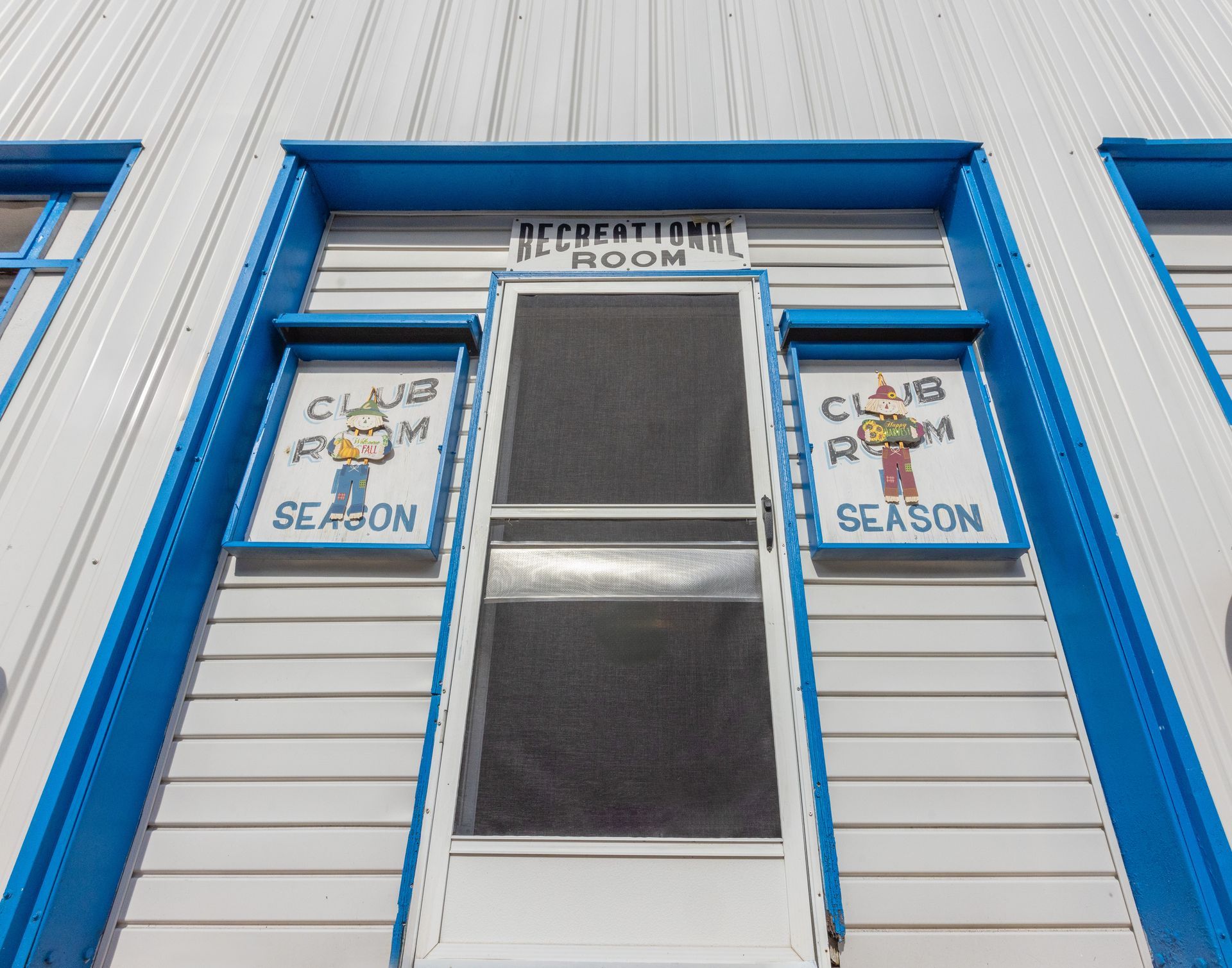 Exterior door to a recreational room with blue trim, white siding, and "Club Room Season" signs.