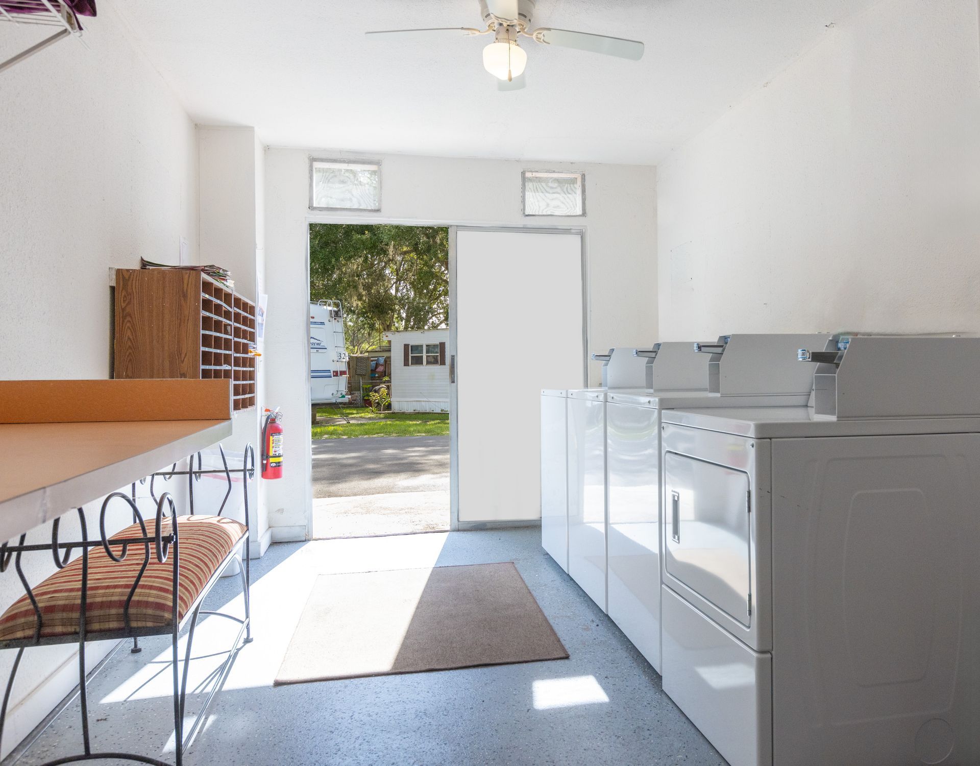 Laundry room with washers, dryers, folding table, and open door to the outside.