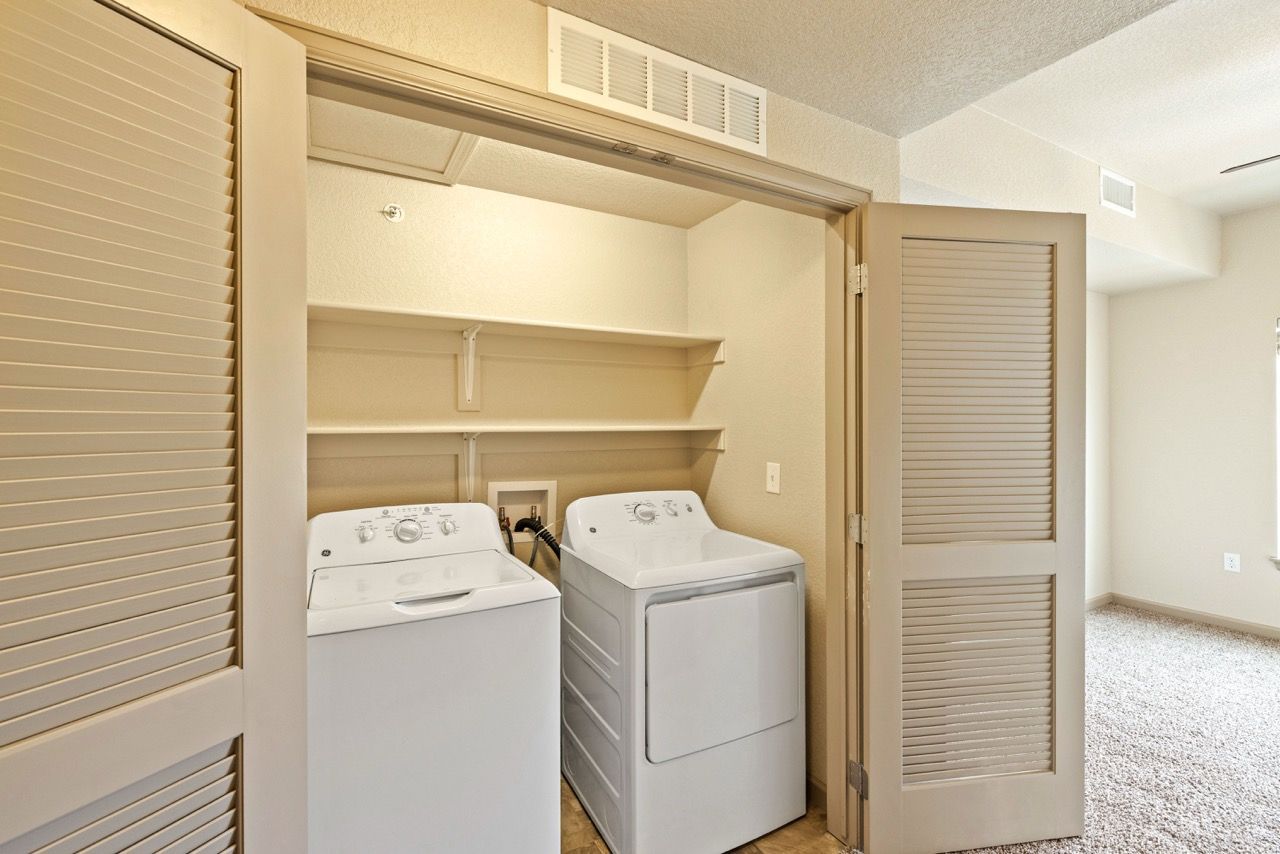 In-unit laundry closet with washer and dryer, open shelves, beige bi-fold doors.