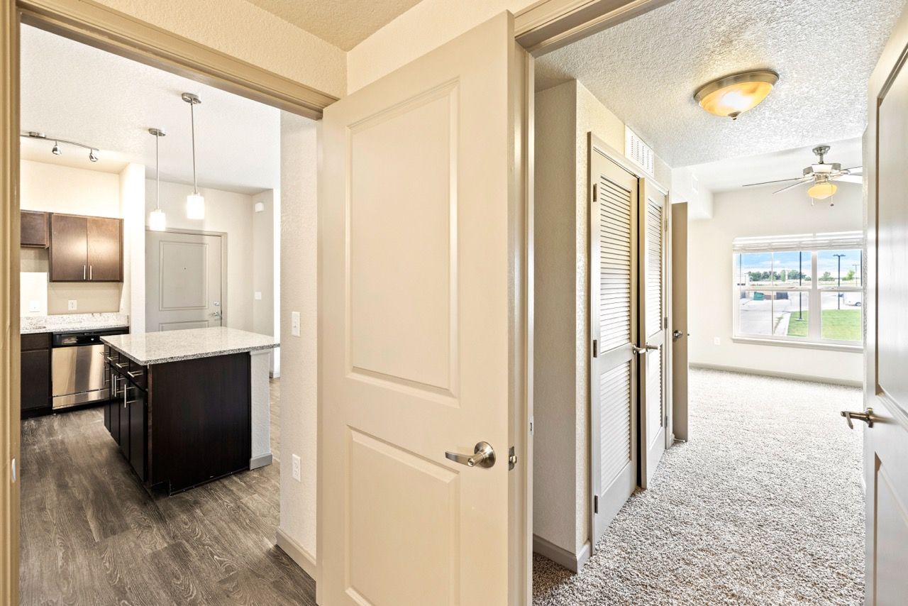 Open-concept apartment interior: kitchen with island, pendant lights, and carpeted living area