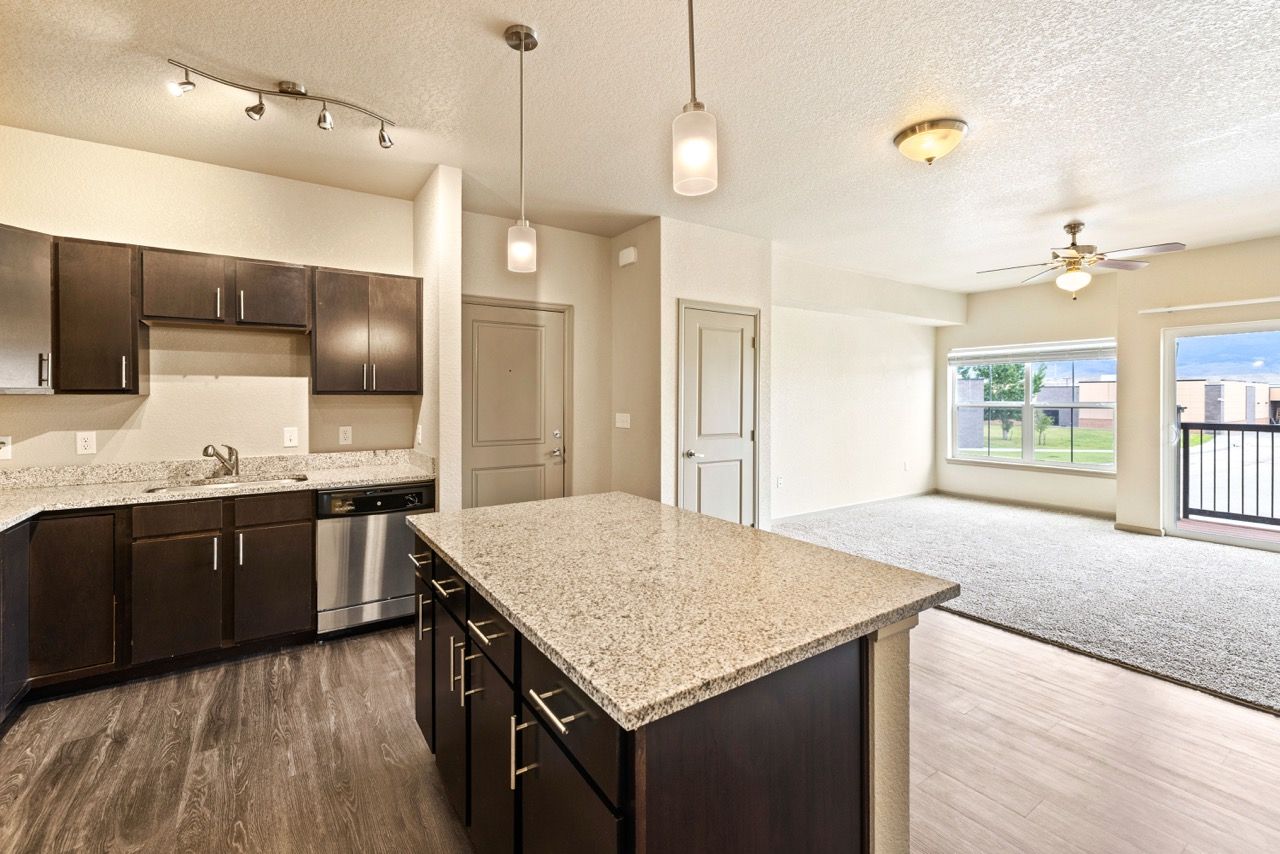 Open-concept kitchen with granite island, dark wood cabinets, and a bright living area with a large window.
