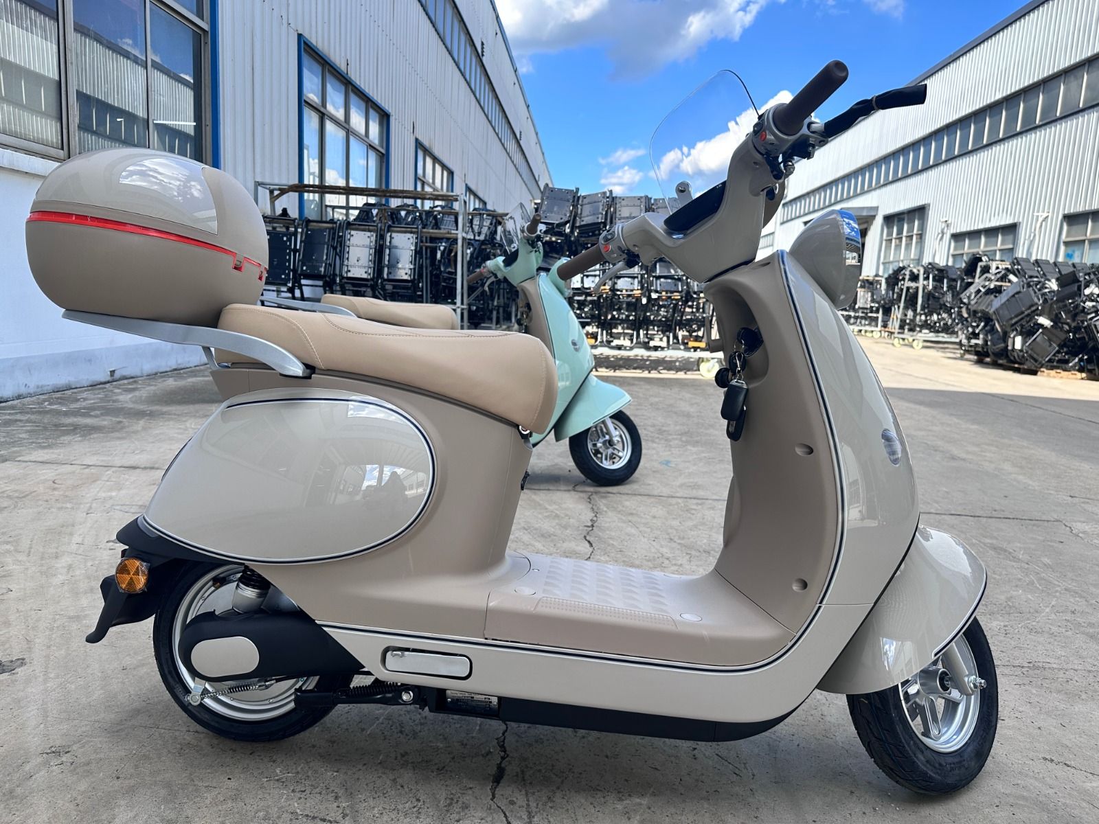 Patinete eléctrico de color beige con maleta superior a juego, aparcado en el exterior de un edificio.