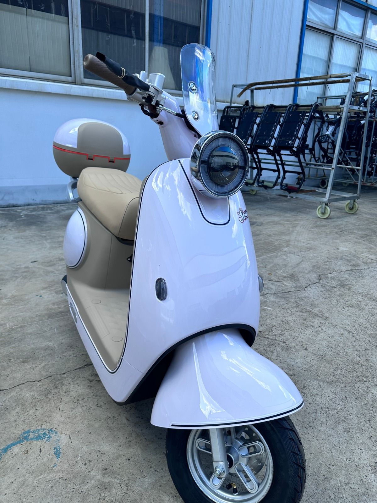 Patinete eléctrico de color rosa y tostado con parabrisas, faro redondo y asiento tostado, estacionado en el exterior.