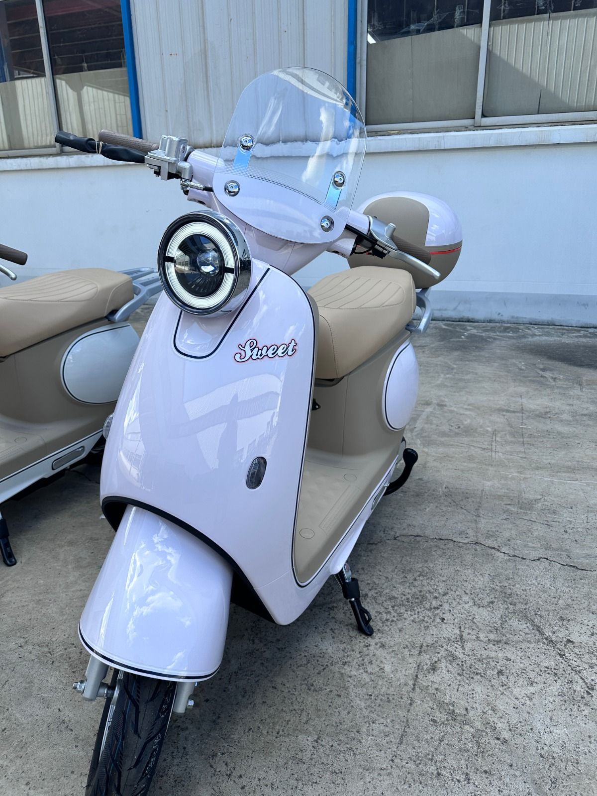 Scooter vintage de color rosa y tostado con parabrisas, estacionado sobre una superficie de concreto.