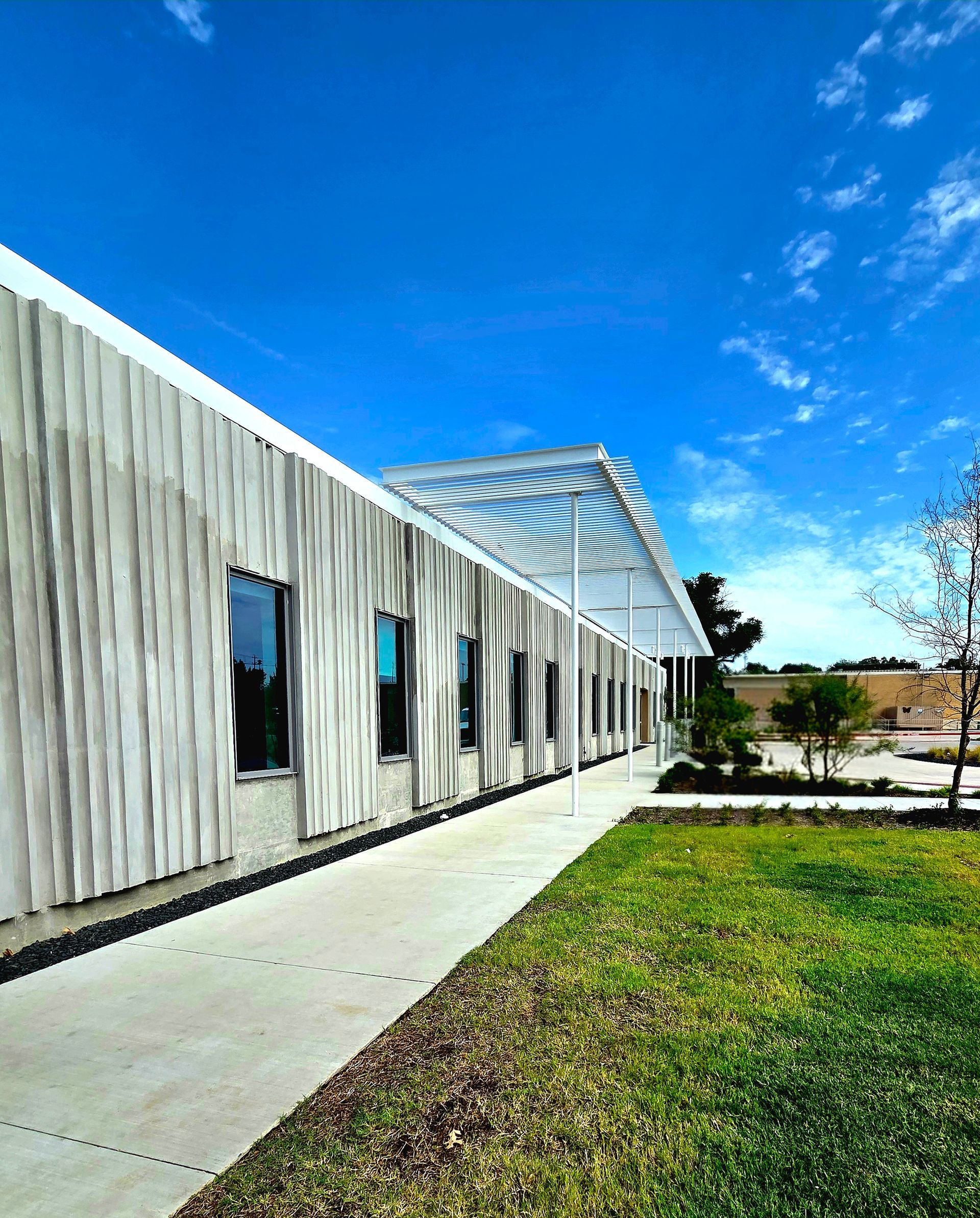 Modern building with textured gray facade and covered walkway, against a bright blue sky.