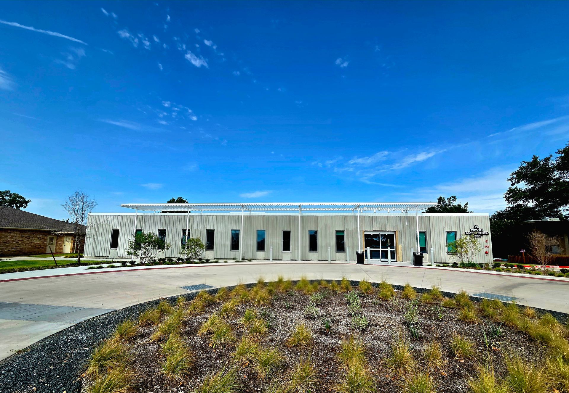 Modern building with vertical gray siding, surrounded by landscaping, under a blue sky.