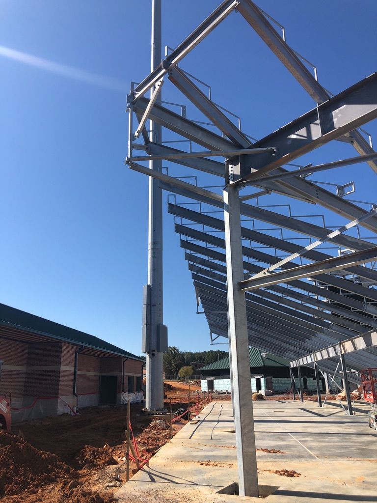 Construction site with steel framework and a tall pole against a blue sky.