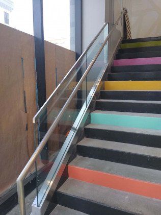 Staircase with colorful risers and glass and metal railing.