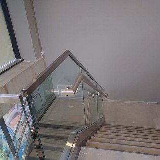 Staircase with glass and metal railing, leading downwards. Gray walls and flooring.