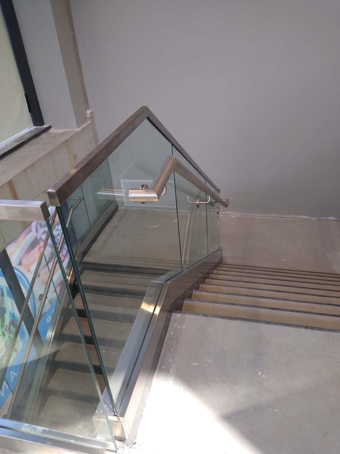 Staircase with glass and metal railing, concrete steps, and a wooden handrail.