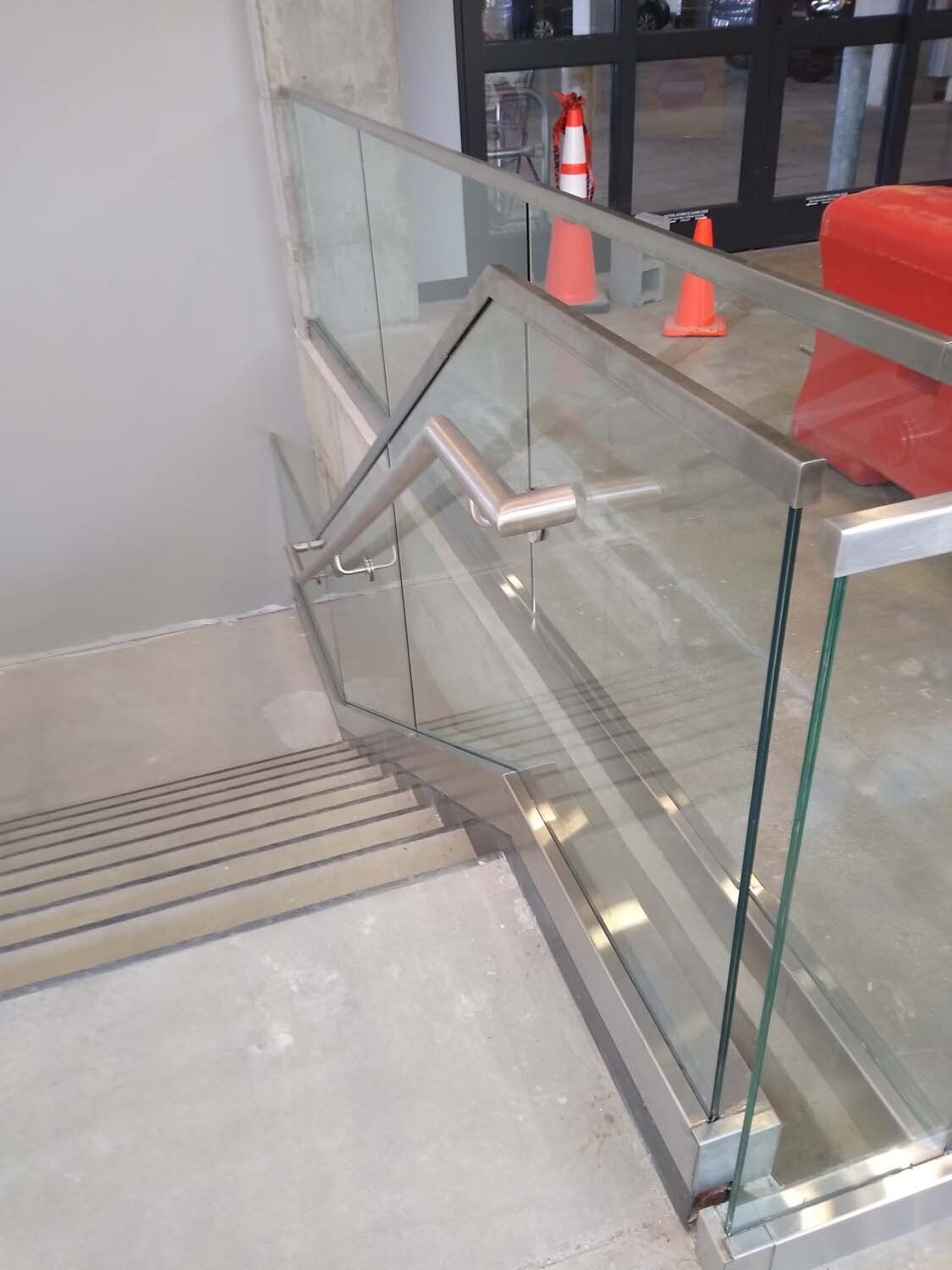 Staircase with stainless steel handrails and glass panels. Concrete steps and landing.