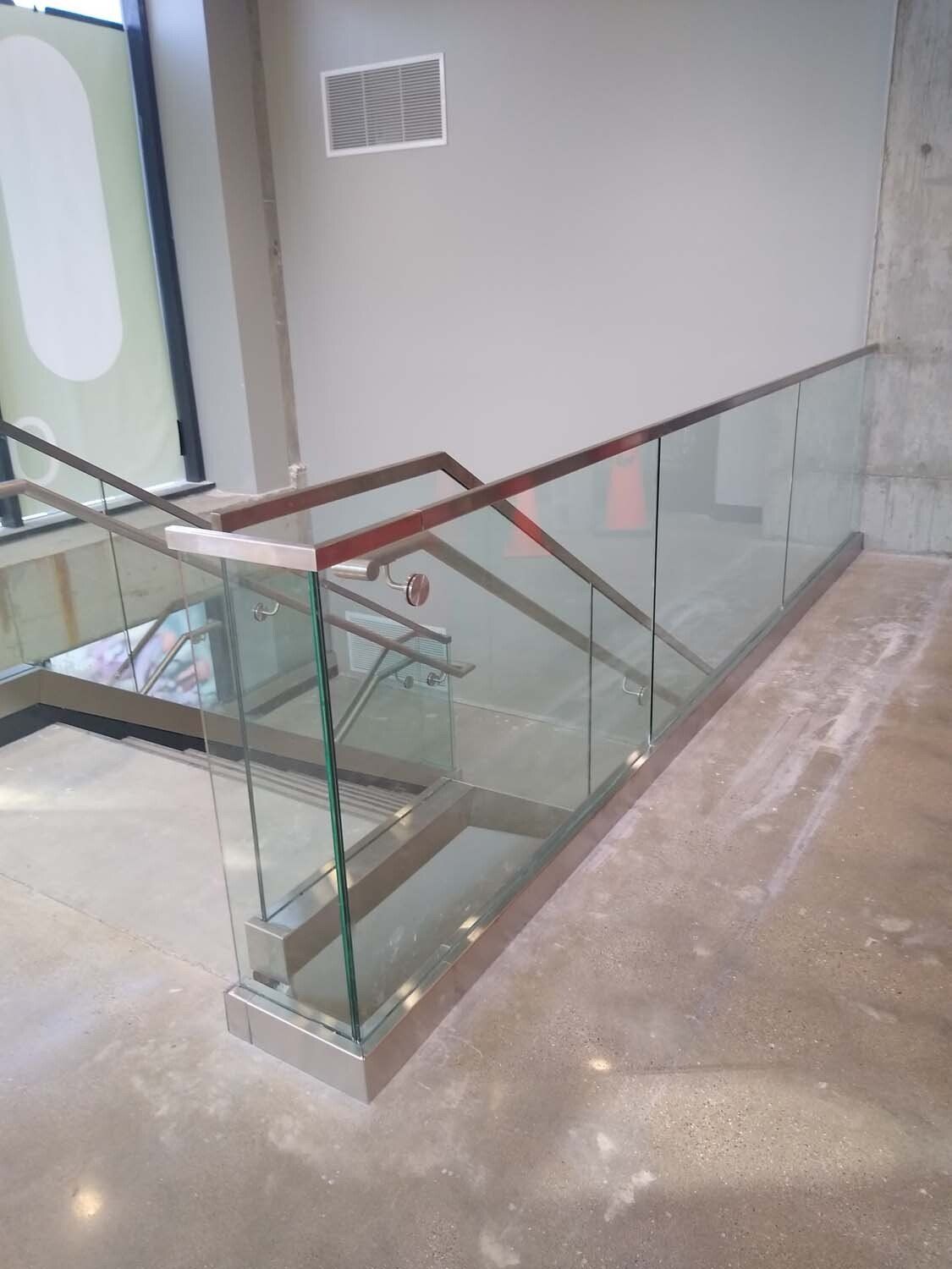 Staircase with glass railing, metal handrail, and concrete steps.