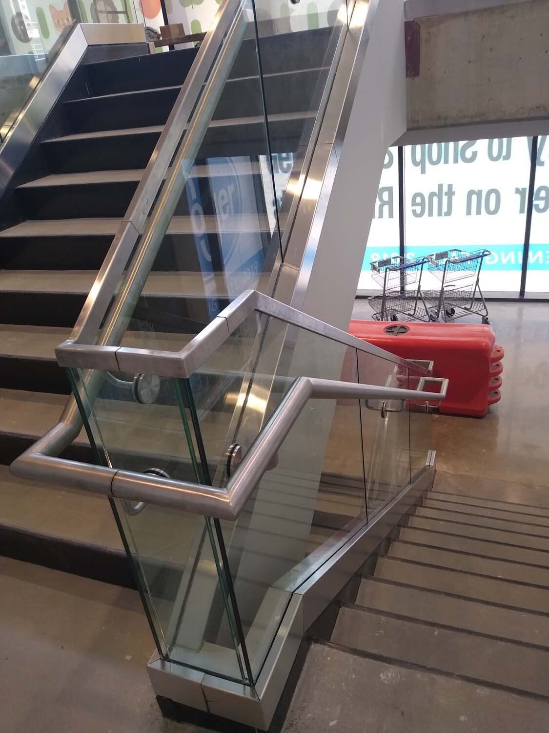 Staircase with glass railing and black steps. A red container is nearby.