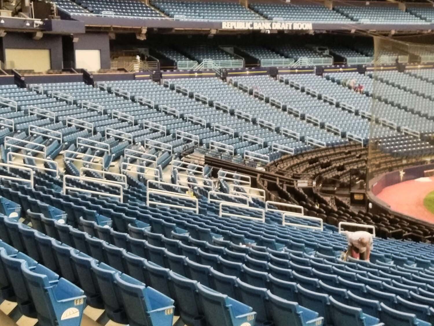 Empty stadium seats, mostly blue, with a person working in the stands.