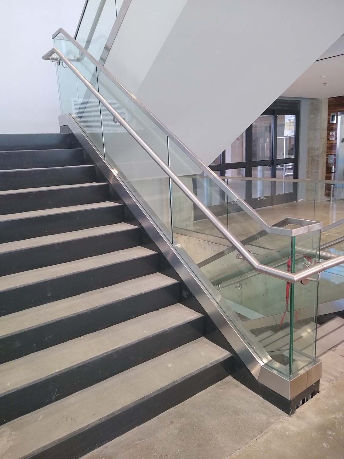 Staircase with glass panels and metal handrails. The stairs are dark gray.