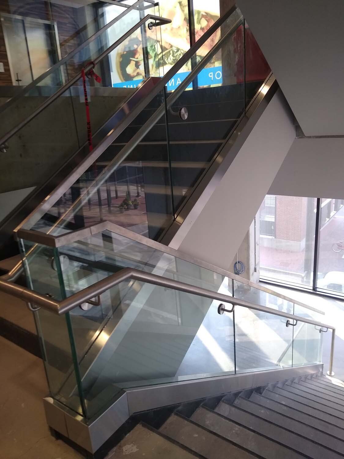 Staircase with glass and metal railings. Gray concrete steps lead up and around a corner.