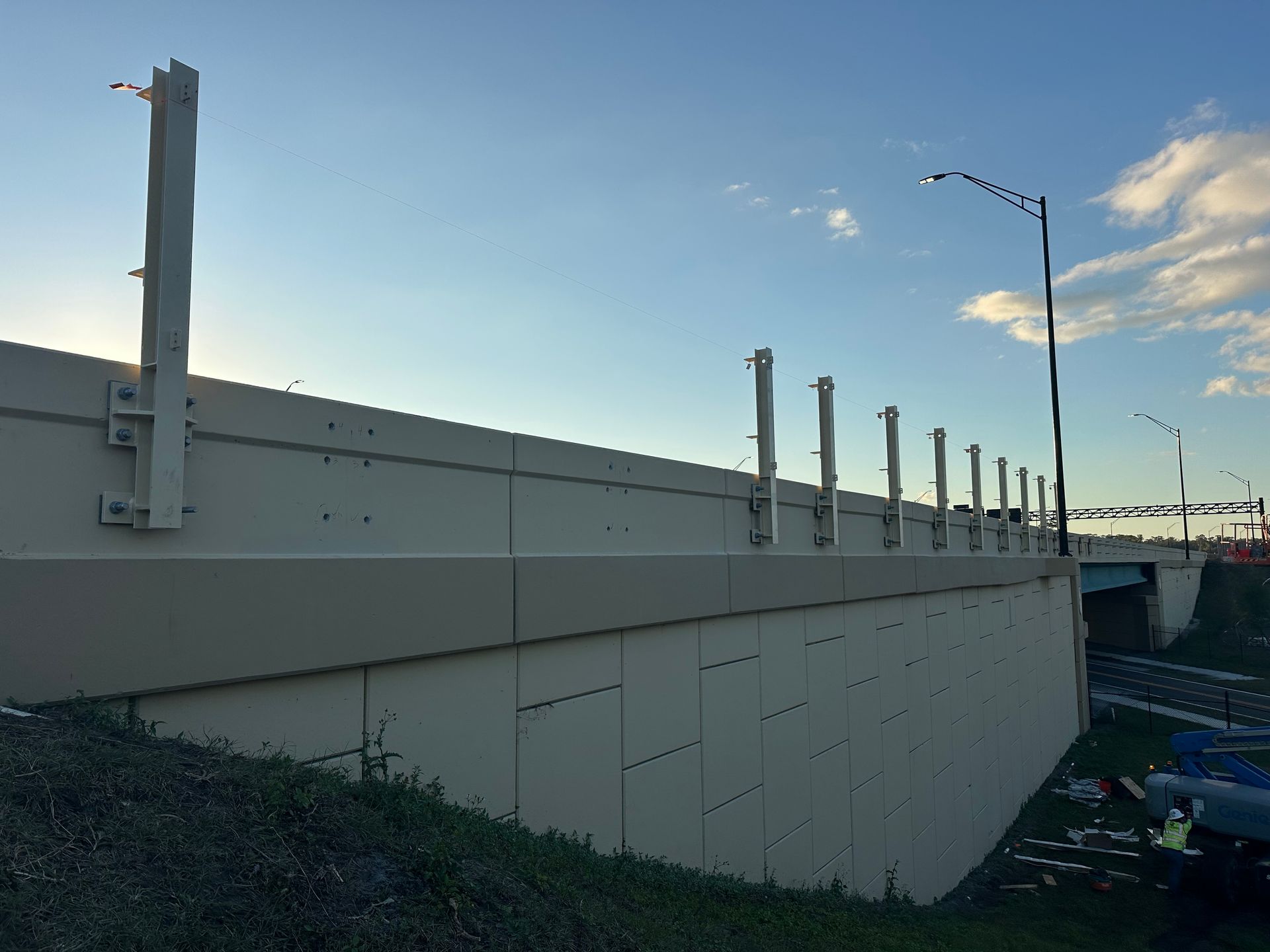 Concrete bridge side with metal supports and a streetlight under a blue sky.
