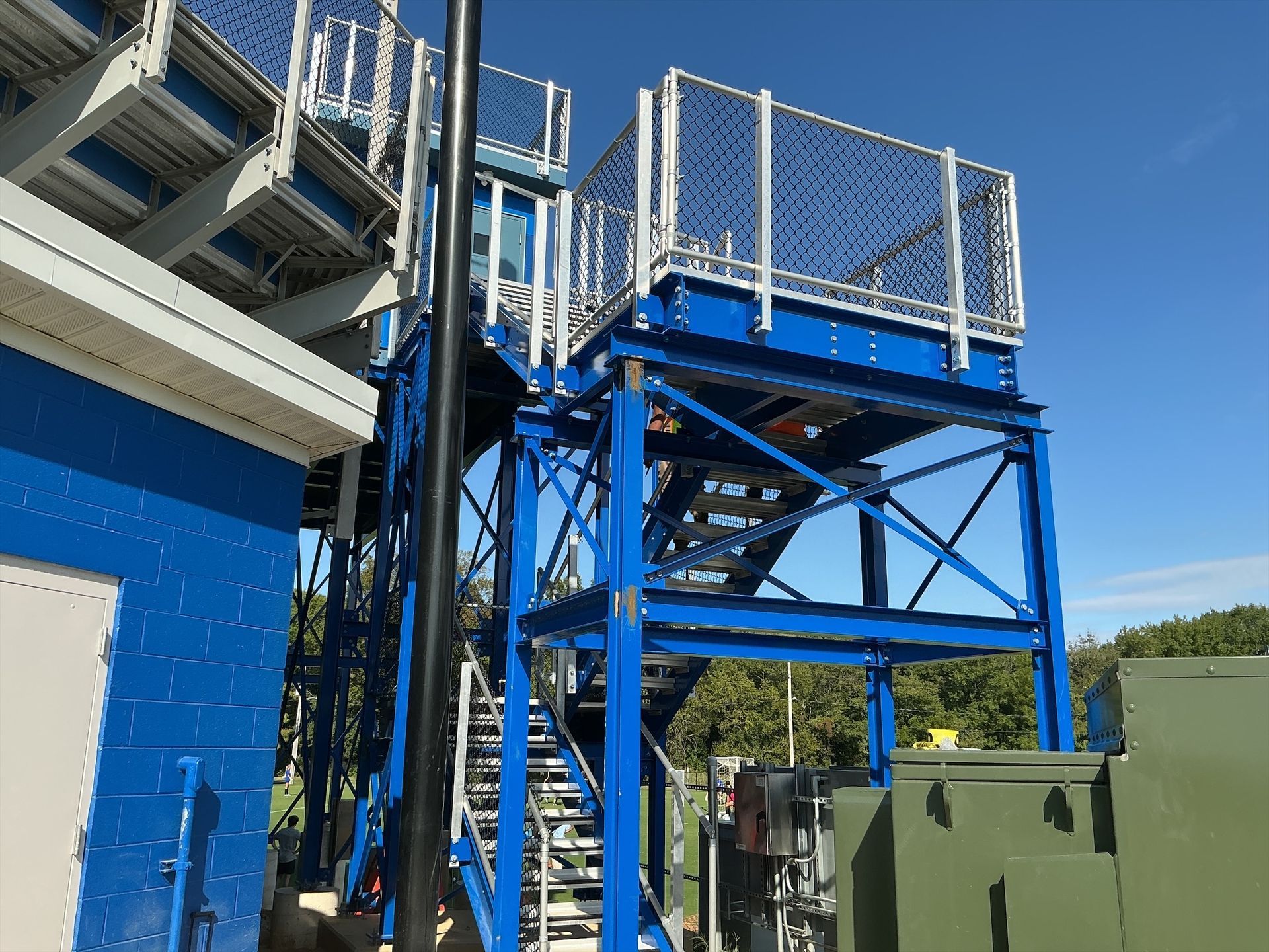 Blue metal staircase and platform next to a building, under a blue sky.