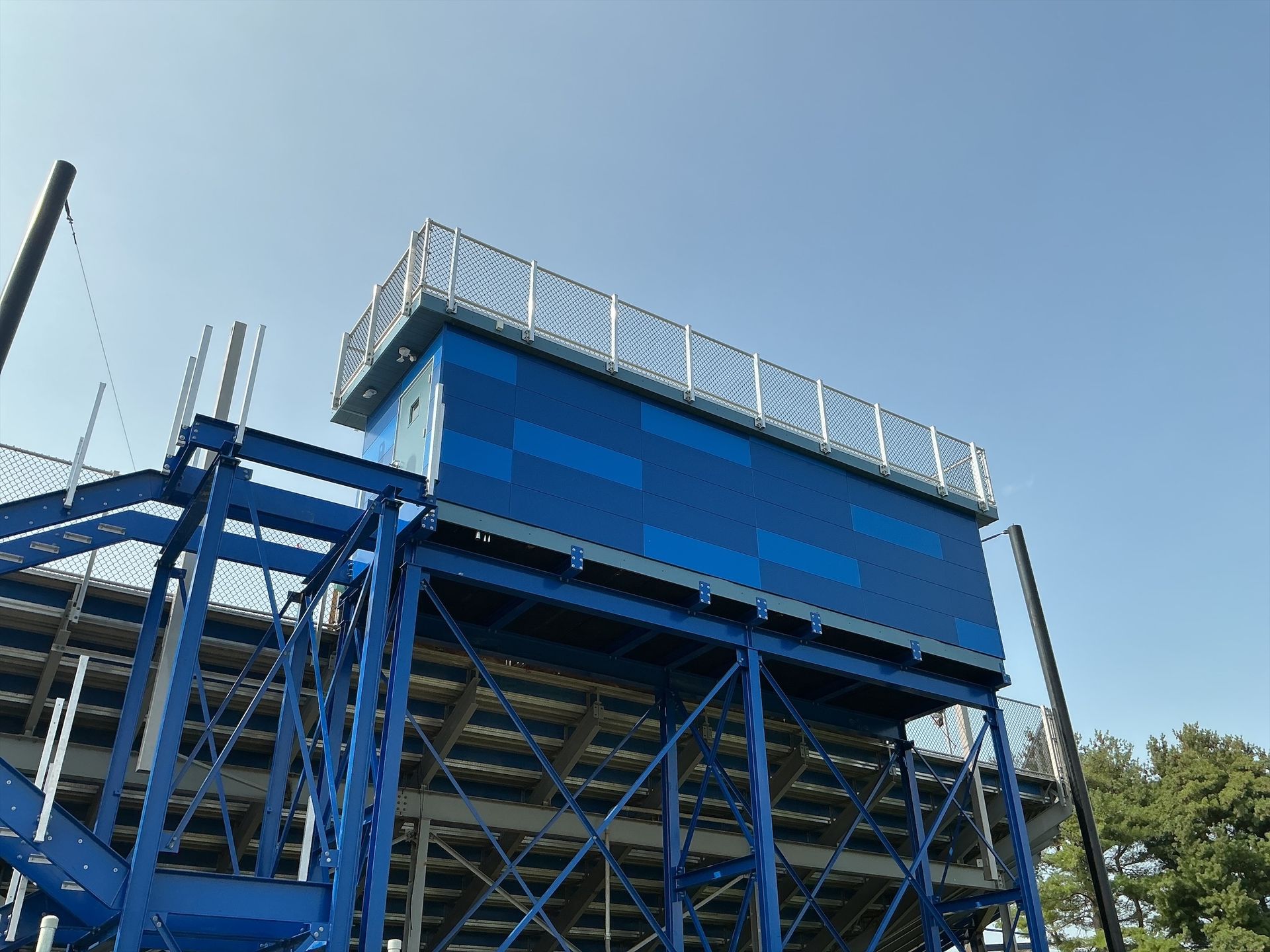 Blue industrial structure with stairs, handrails, and electrical boxes against a blue sky.