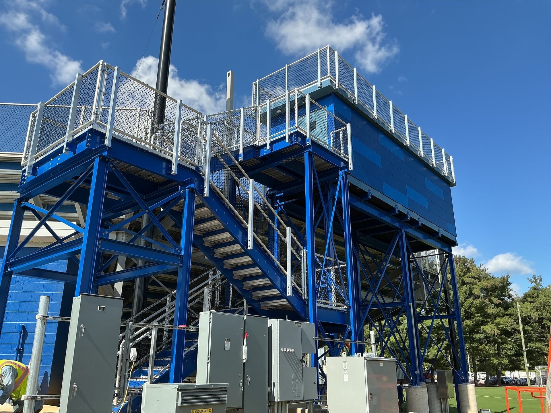 Blue metal industrial structure with stairs, platform, and safety railings against a blue sky.