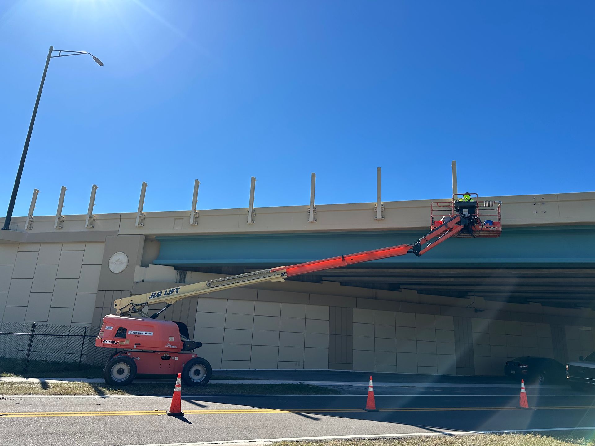 A worker in a boom lift repairs a concrete overpass. Sunny, clear sky.