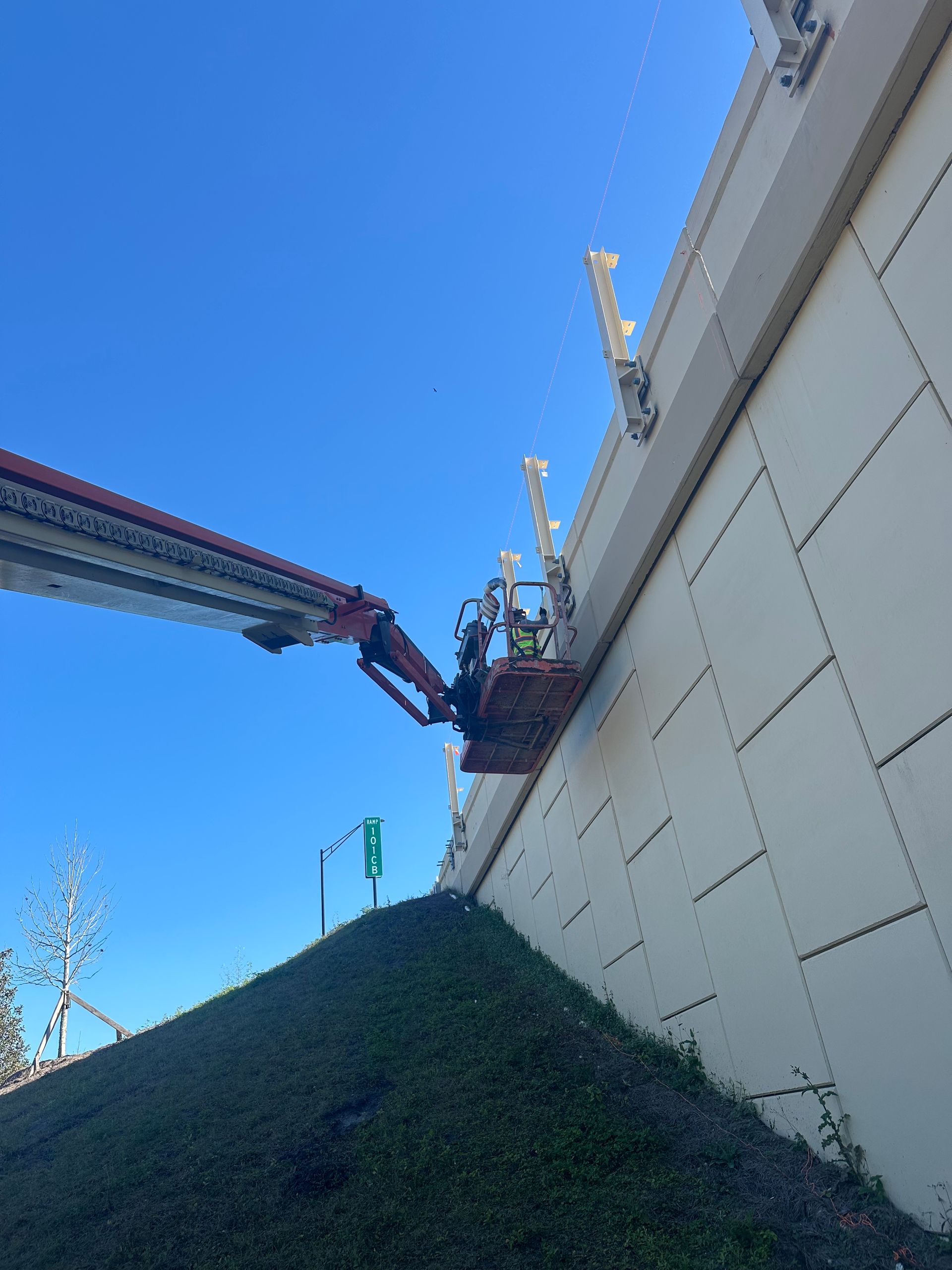 Person in a lift basket working on a wall, clear blue sky overhead.
