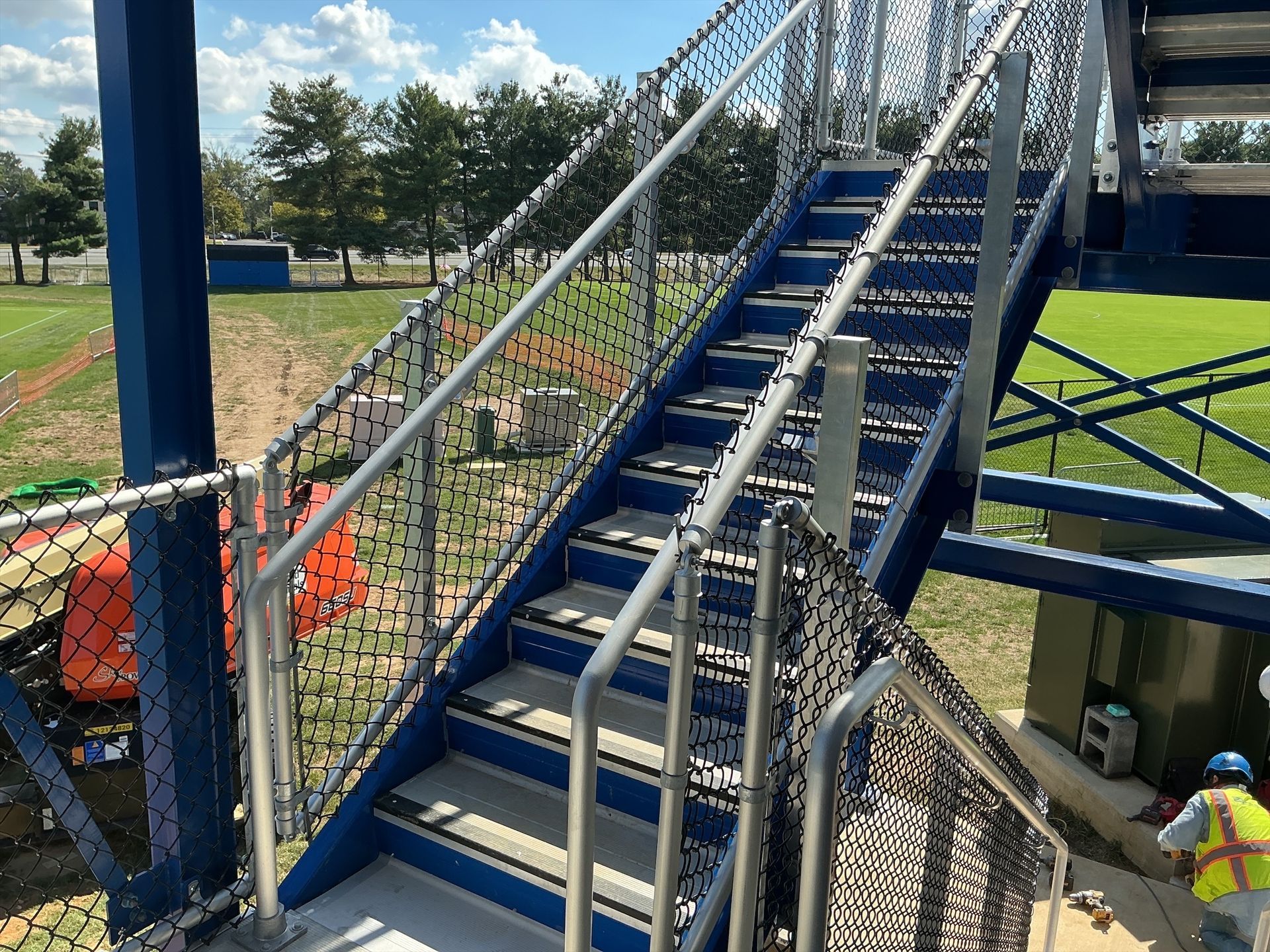 Blue metal stadium stairs with silver handrails and chain link safety netting.