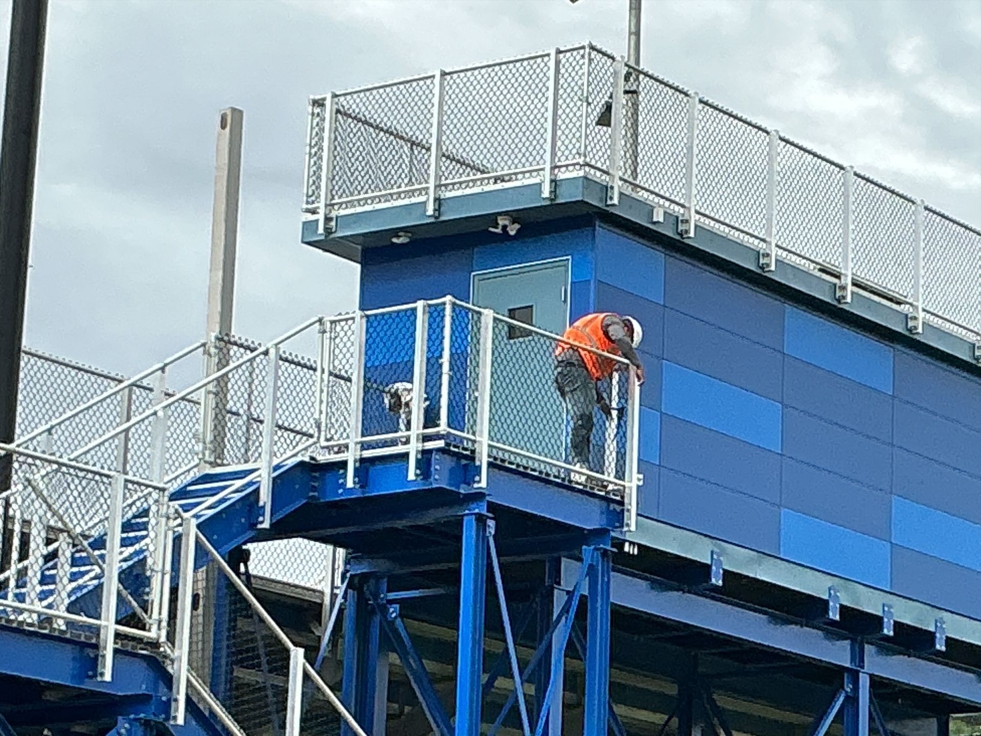 Blue industrial structure with stairs, handrails, and electrical boxes against a blue sky.