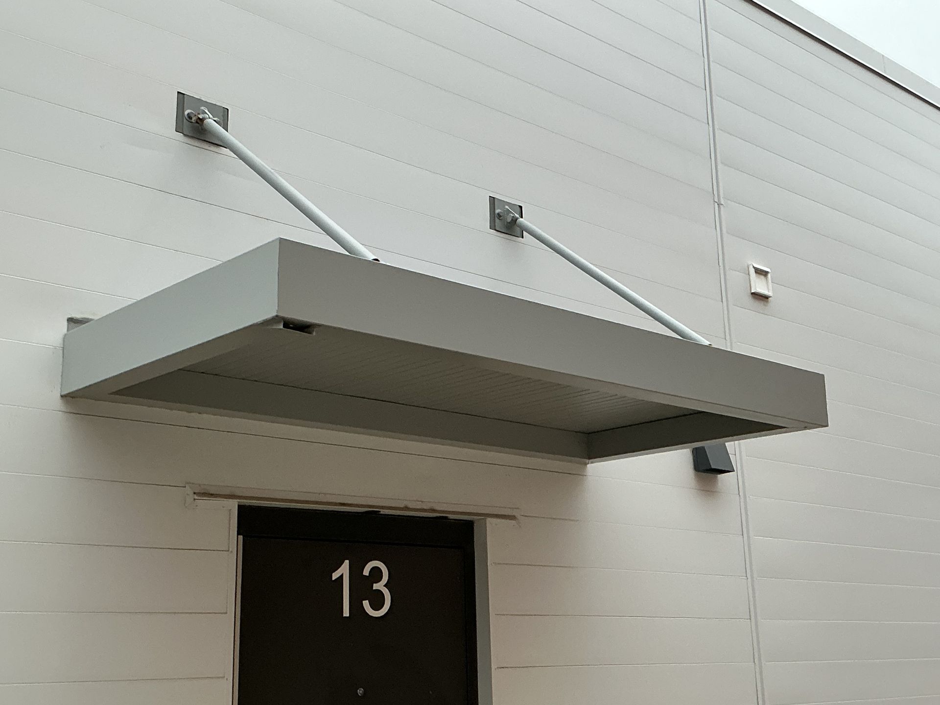 Exterior of a building with a metal awning and a walkway. Cloudy sky above.
