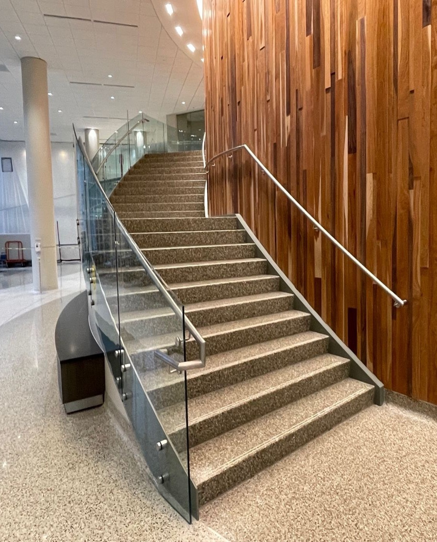 Staircase with terrazzo steps, glass railings, and wood panel wall.