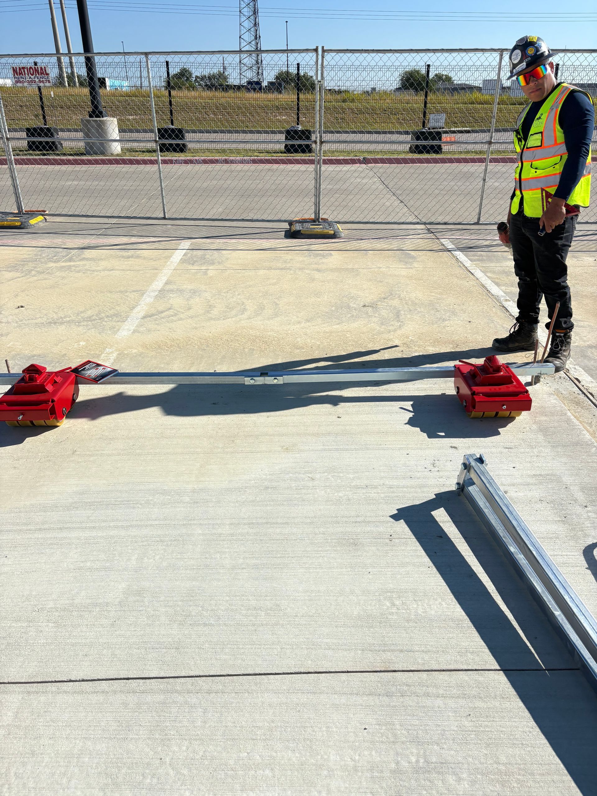 Construction worker in safety vest observing a barrier setup on a concrete surface.