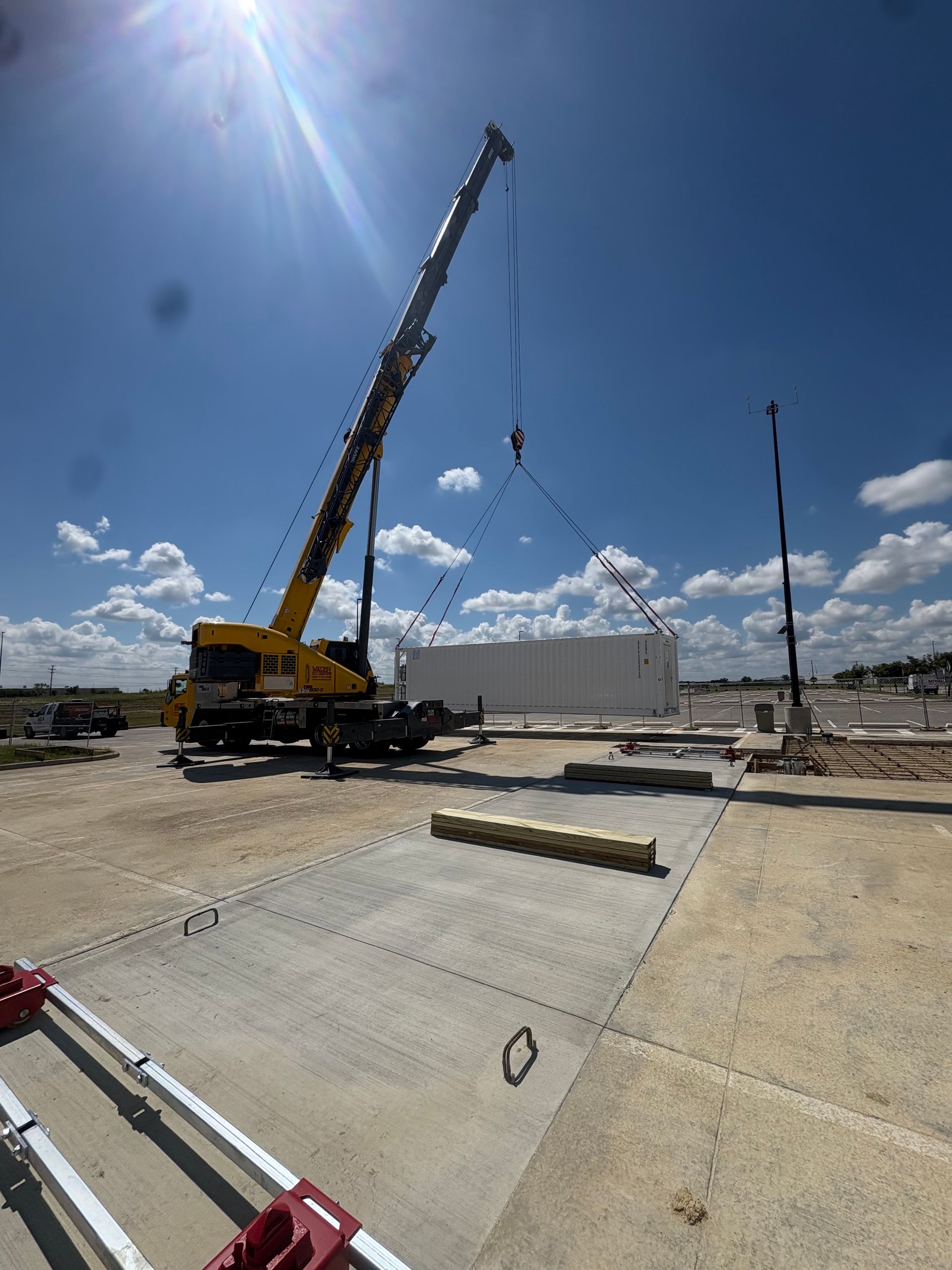 A crane lifting a white shipping container on a construction site under a blue sky.