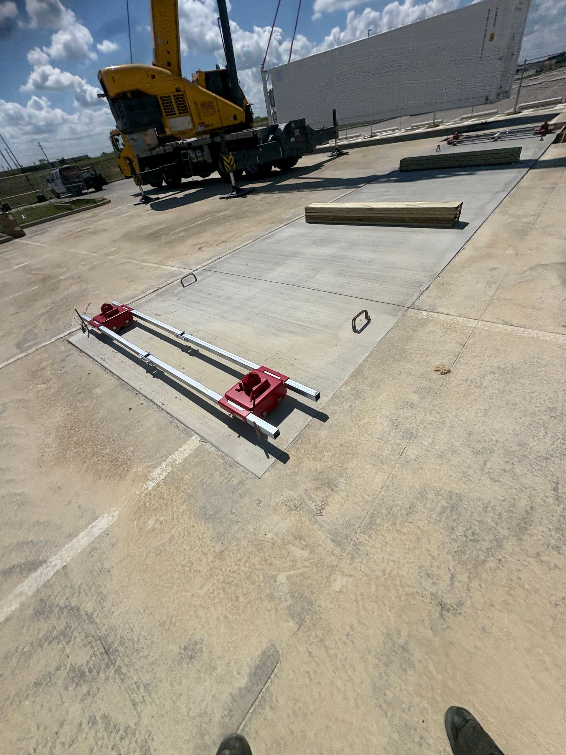 Two red and silver rails on concrete with a crane and large white wall in the background.