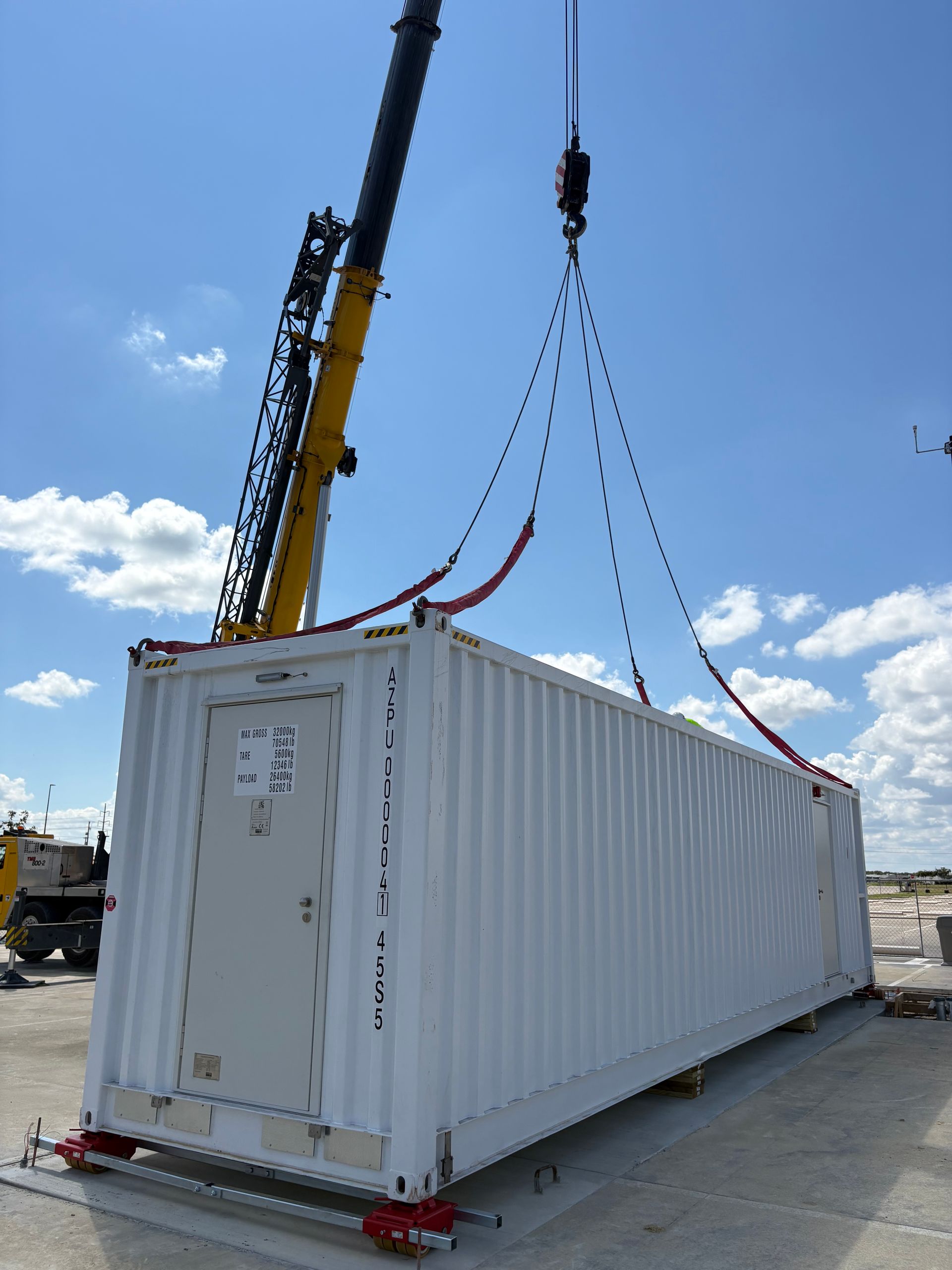 Crane lifting a large white shipping container outdoors.