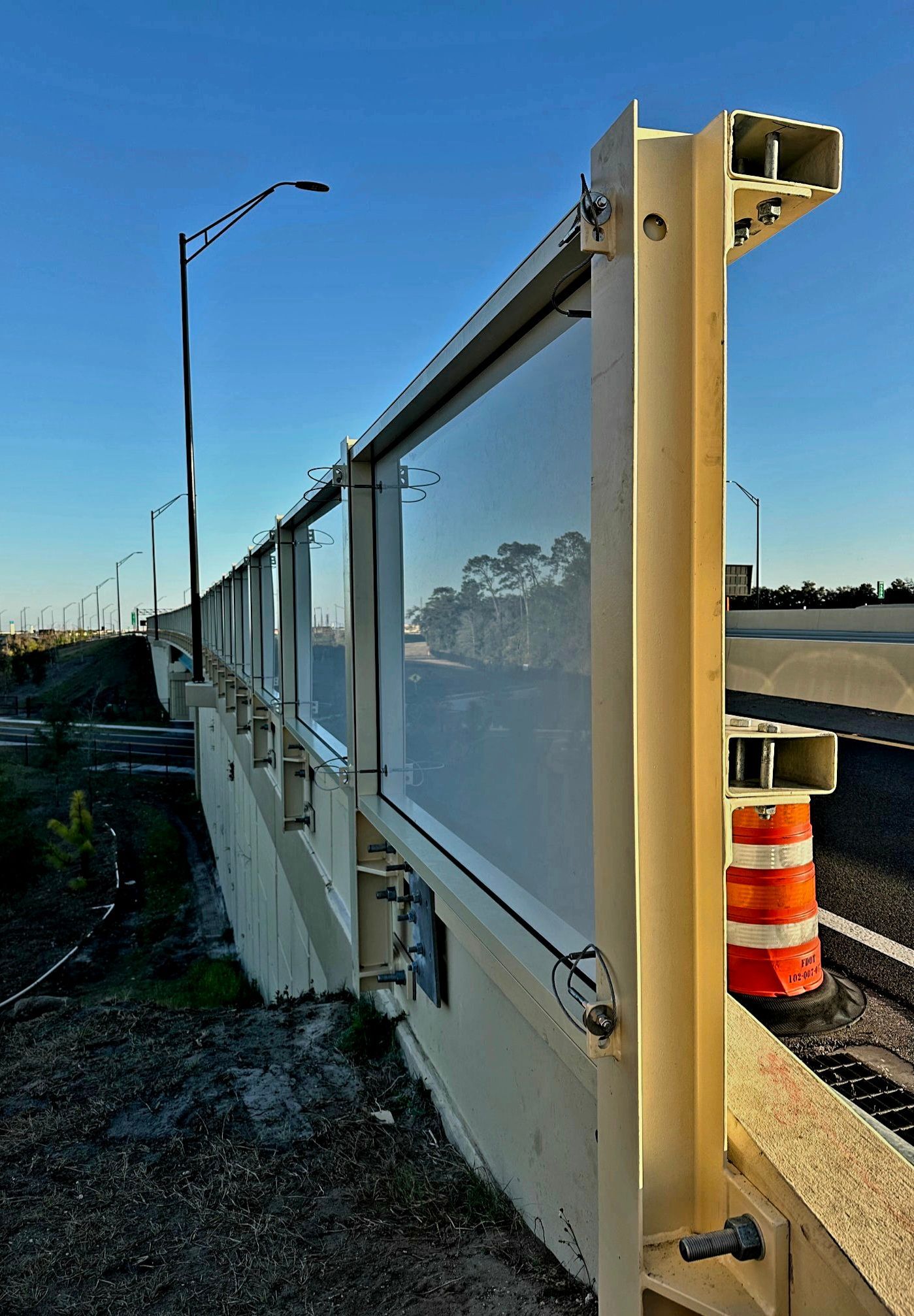 Highway noise barrier with transparent panels and metal framing, against a blue sky.