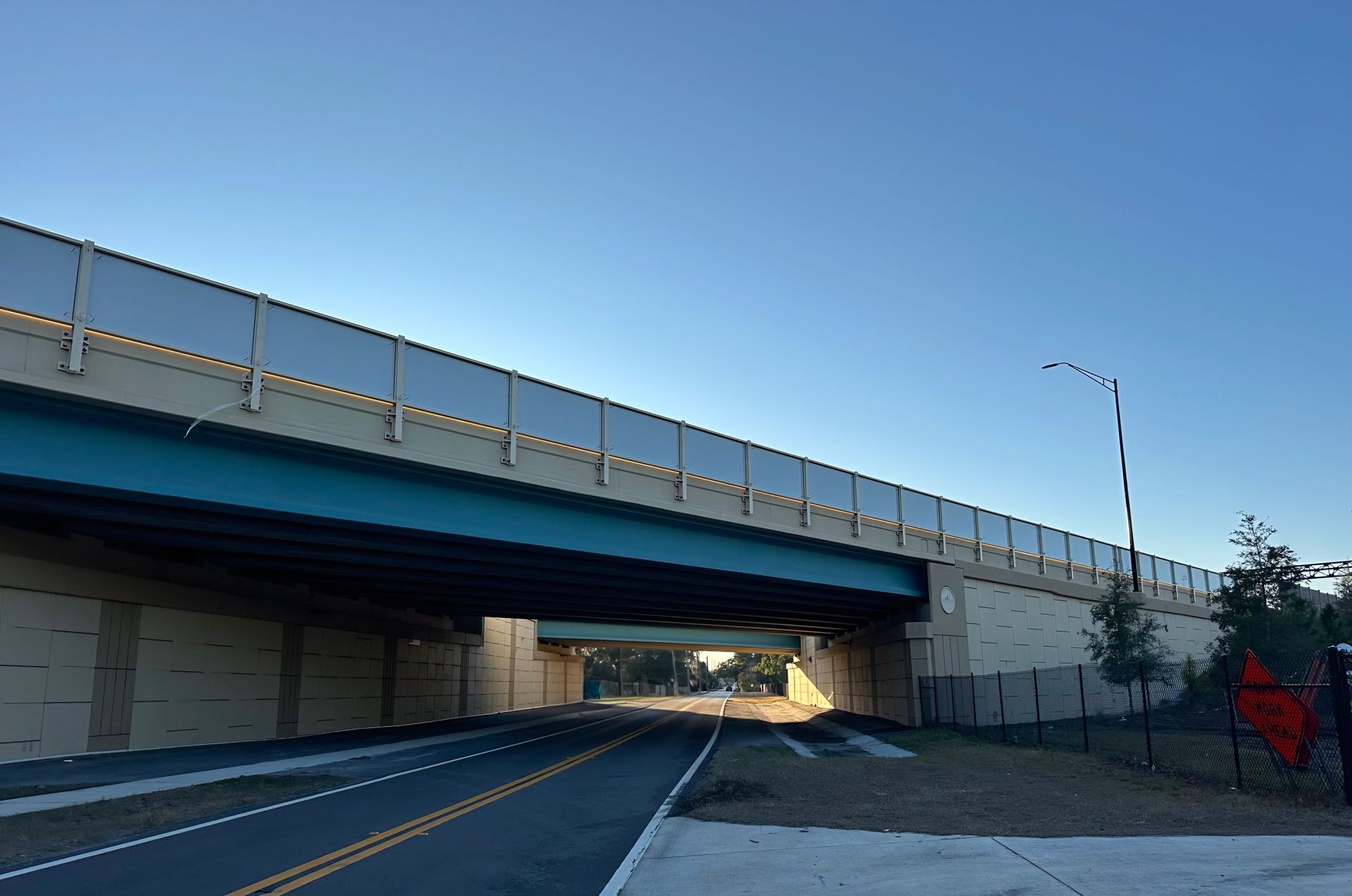 Underpass with a blue underside, asphalt road, and a clear blue sky.