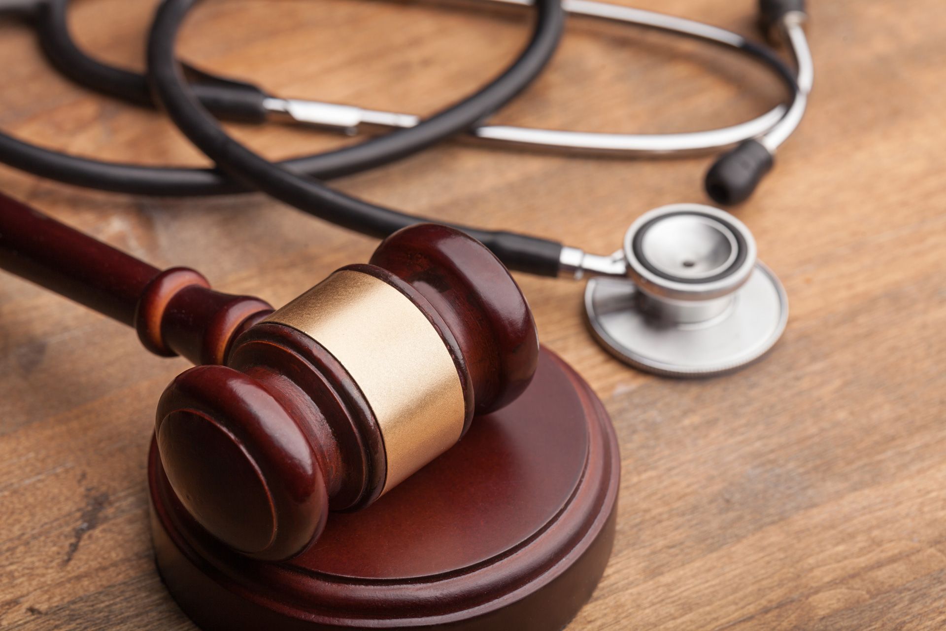 Wooden gavel on stand beside a stethoscope on a wooden surface.