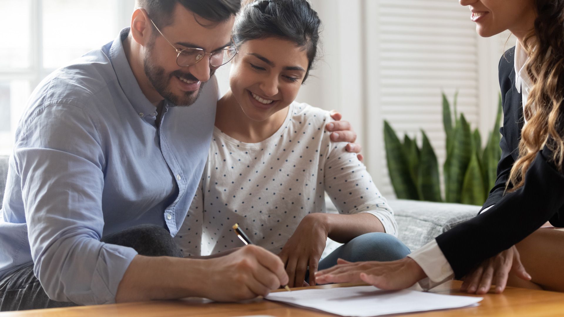 Couple signing documents with a smiling advisor in a bright room.